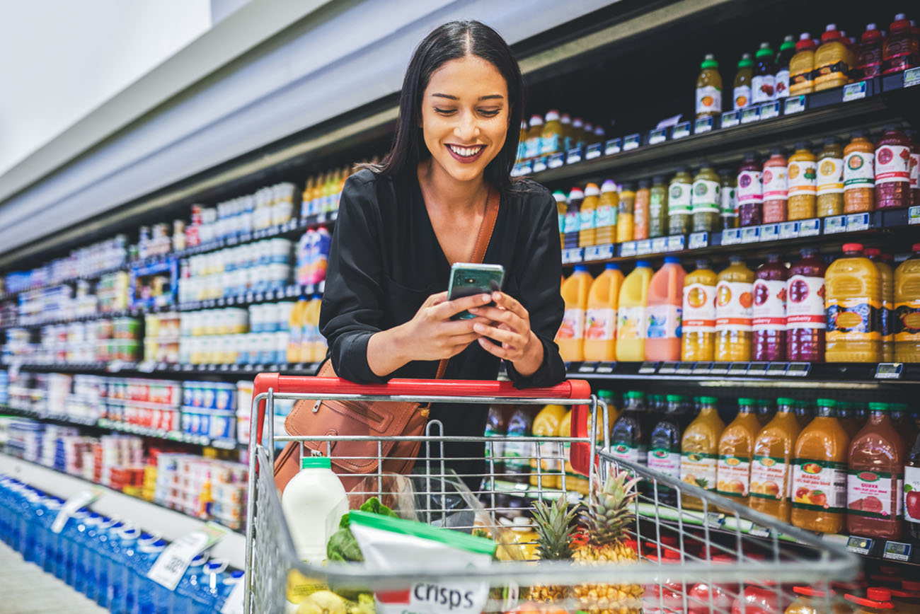 Shot of a young woman using a smartphone while shopping in a grocery store
