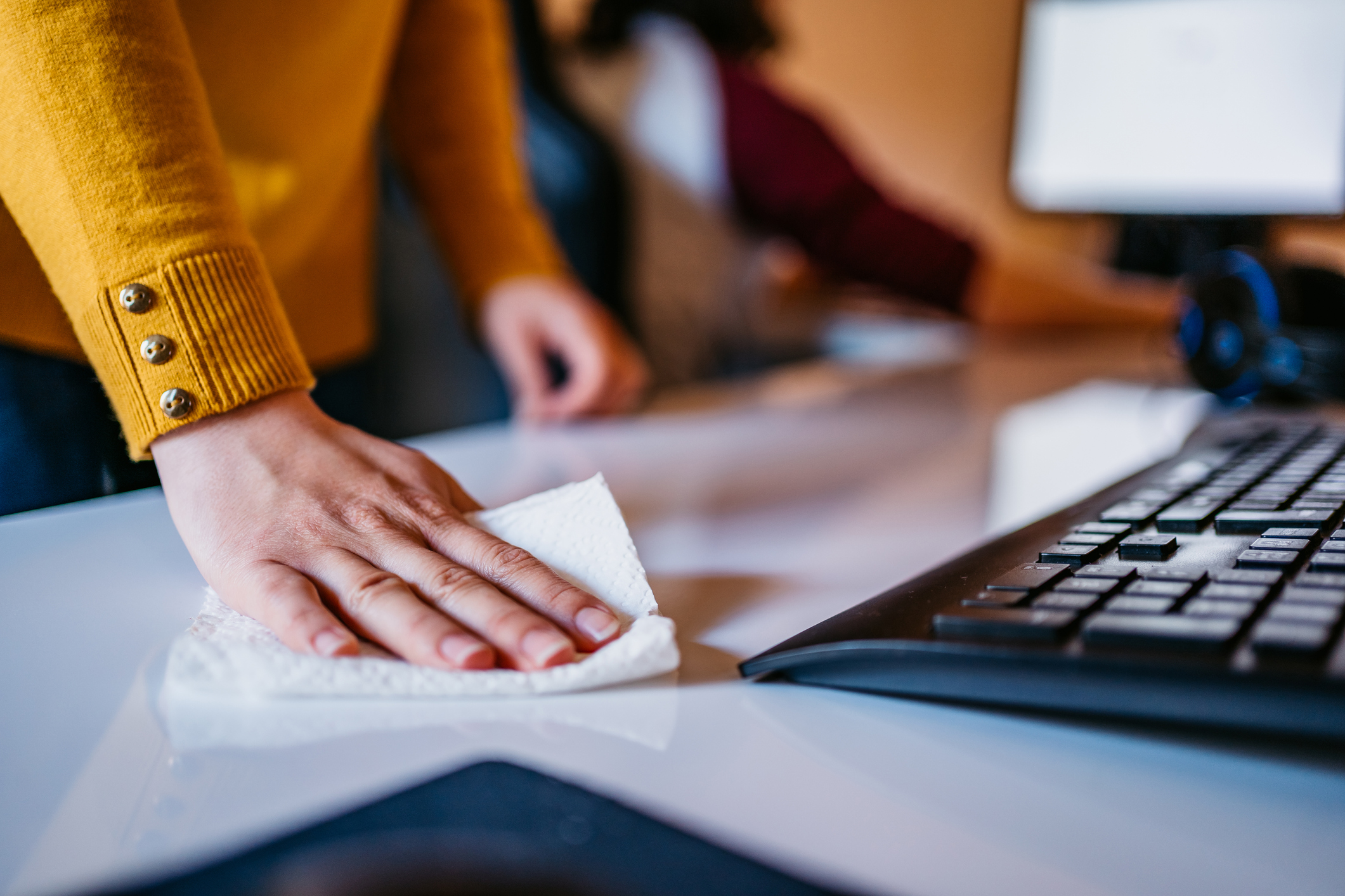 Woman cleaning computer desk in office with wet wipe, close up. She wiping desk with disinfectant disposable wipe.