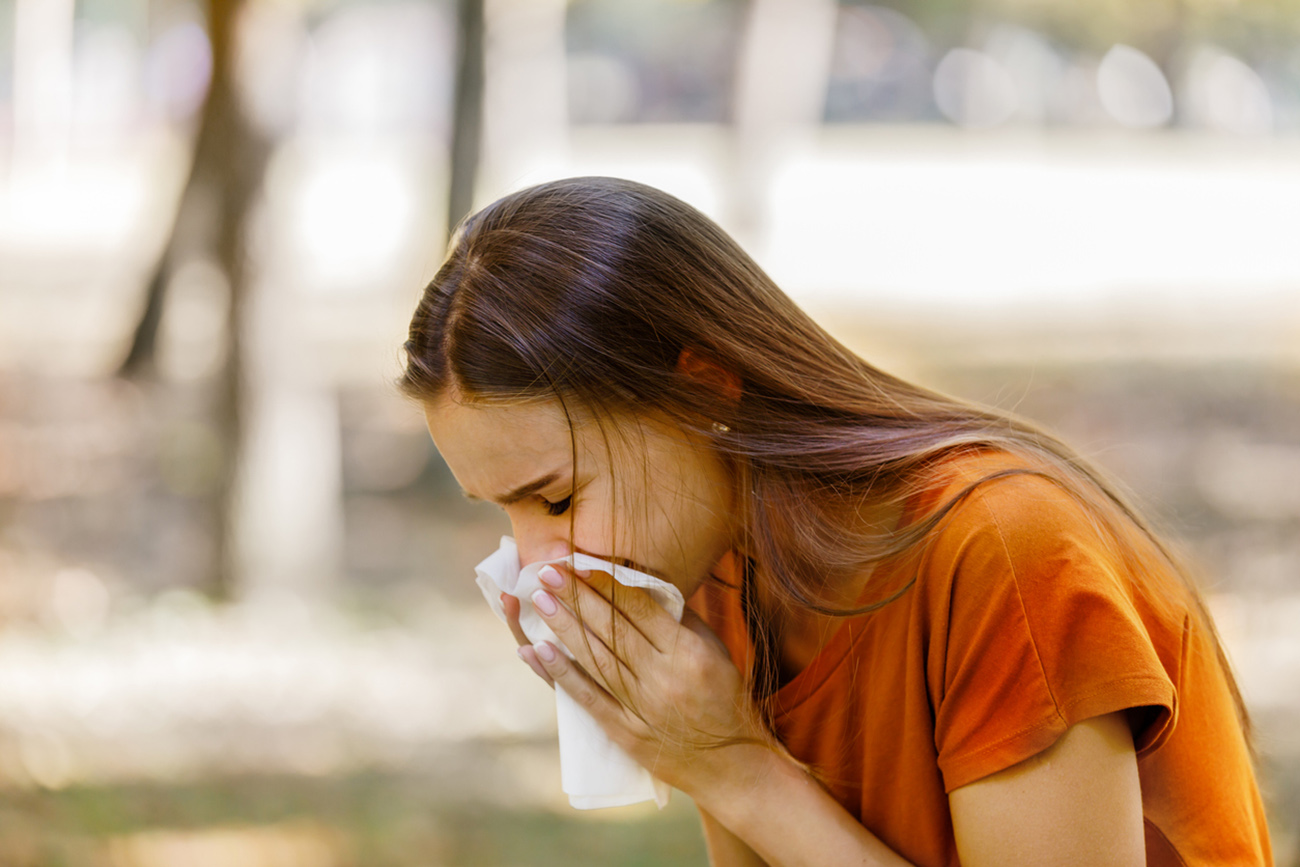 Photo of a Woman With Flu in Public Park Using Facial Tissues While Sneezing Due to Seasonal Flu or Rhinitis.