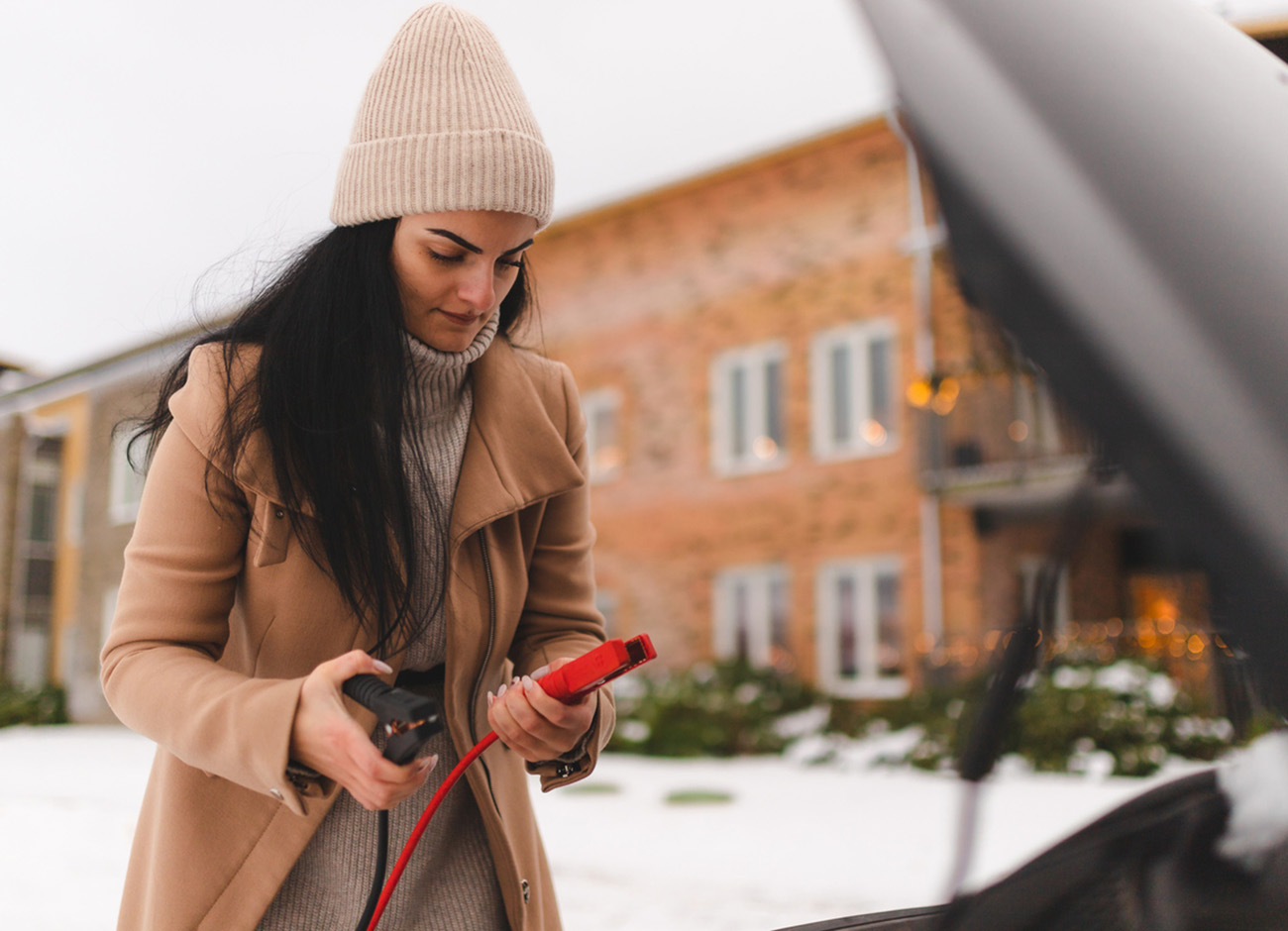 Beautiful young woman trying to figure out how to jump start her car in the winter. Car battery is dead.