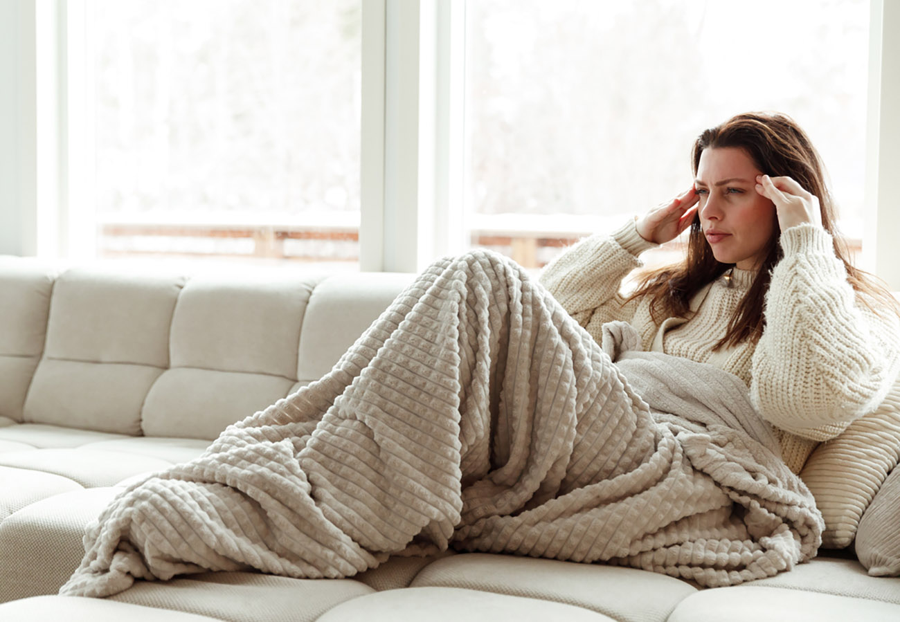 Frustrated young woman suffering from the headache and migraine while sitting on the sofa at home