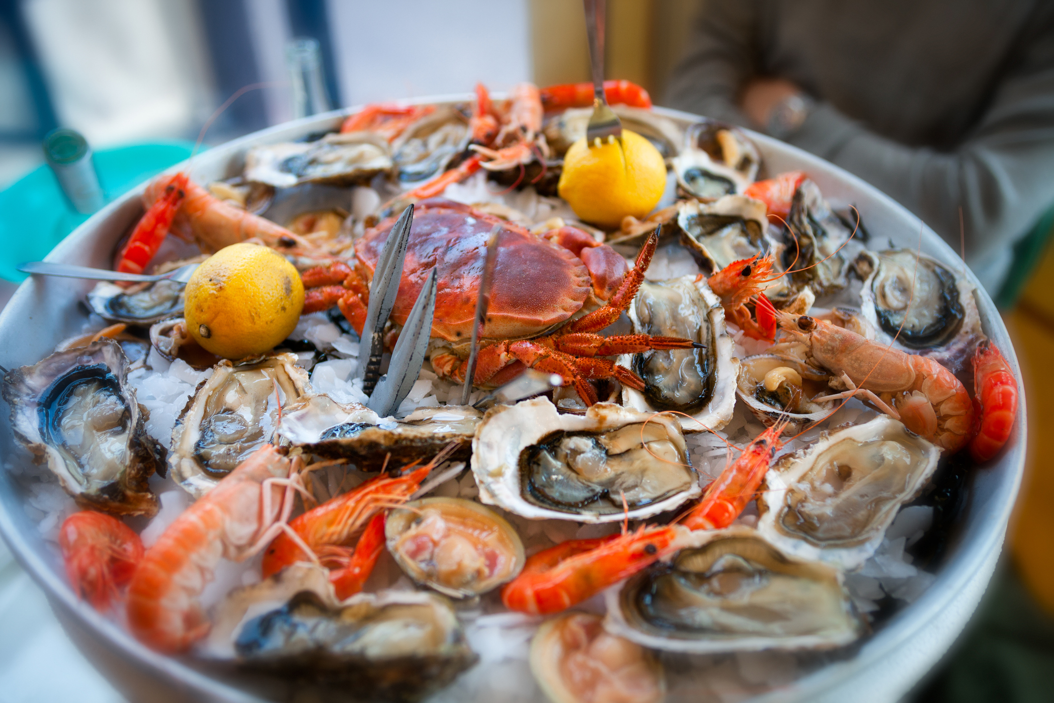 A selection of raw seafood dressed on chipped ice and seaweed in a restaurant in Cannes, France, Springtime.  The selection includes, a mixture of raw oysters, clams, scampi, poached crab and crayfish, garnished with fresh lemons. Seafood is prepared to order to make the platter before it is served.