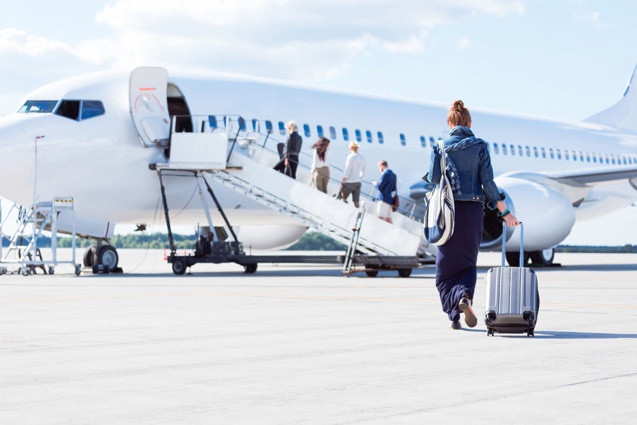 Rear view of young woman with luggage walking towards the airplane. Female traveler going on vacation