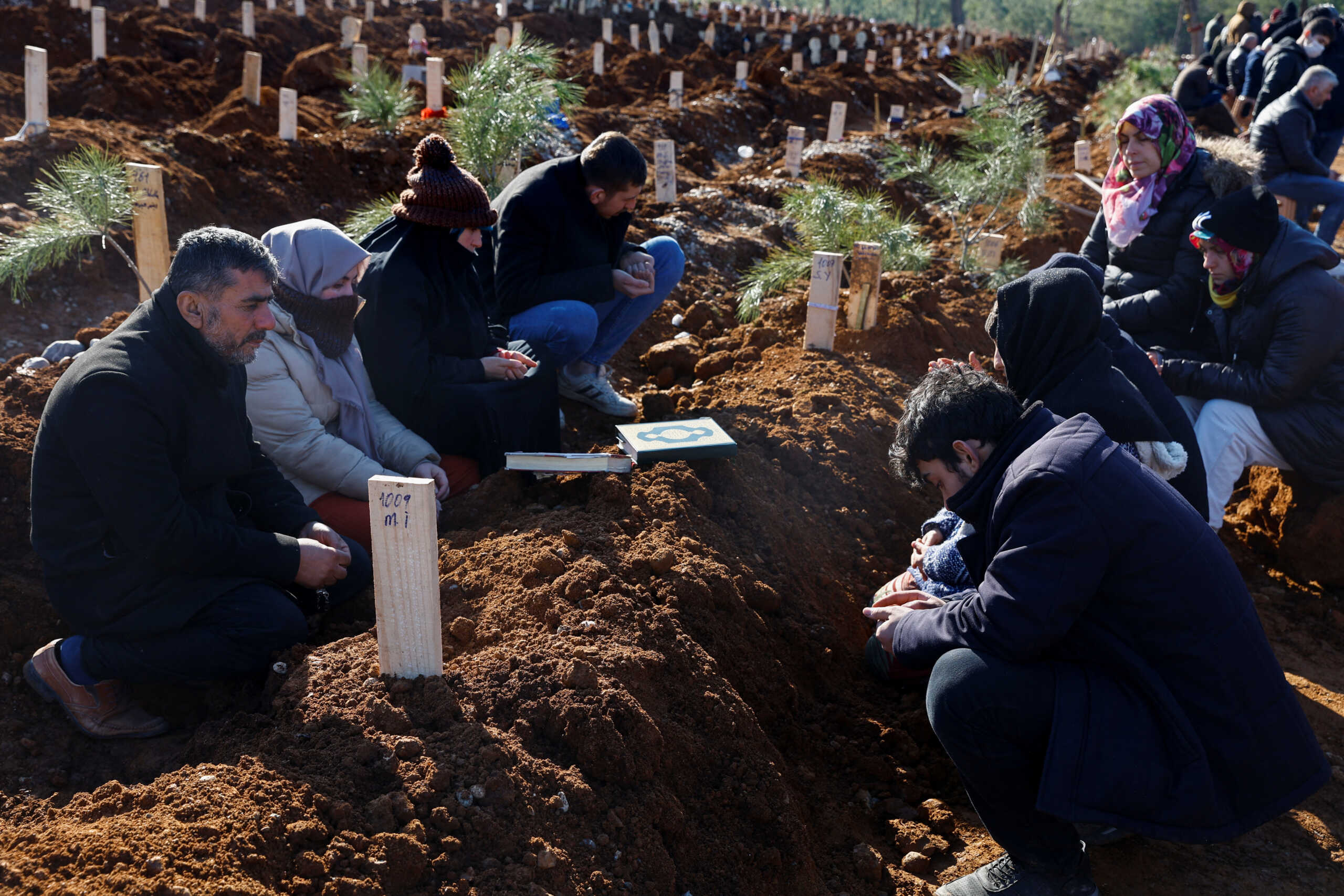 People pray next to the graves of victims of the deadly earthquake, in a cemetery in Kahramanmaras, Turkey February 9, 2023. REUTERS