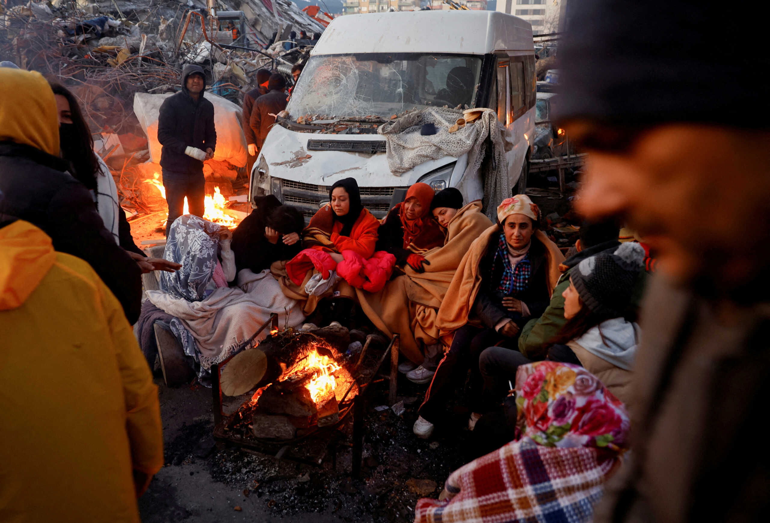 People sit around a fire next to rubble and damages near the site of a collapsed building in the aftermath of an earthquake, in Kahramanmaras, Turkey, February 8, 2023. REUTERS
