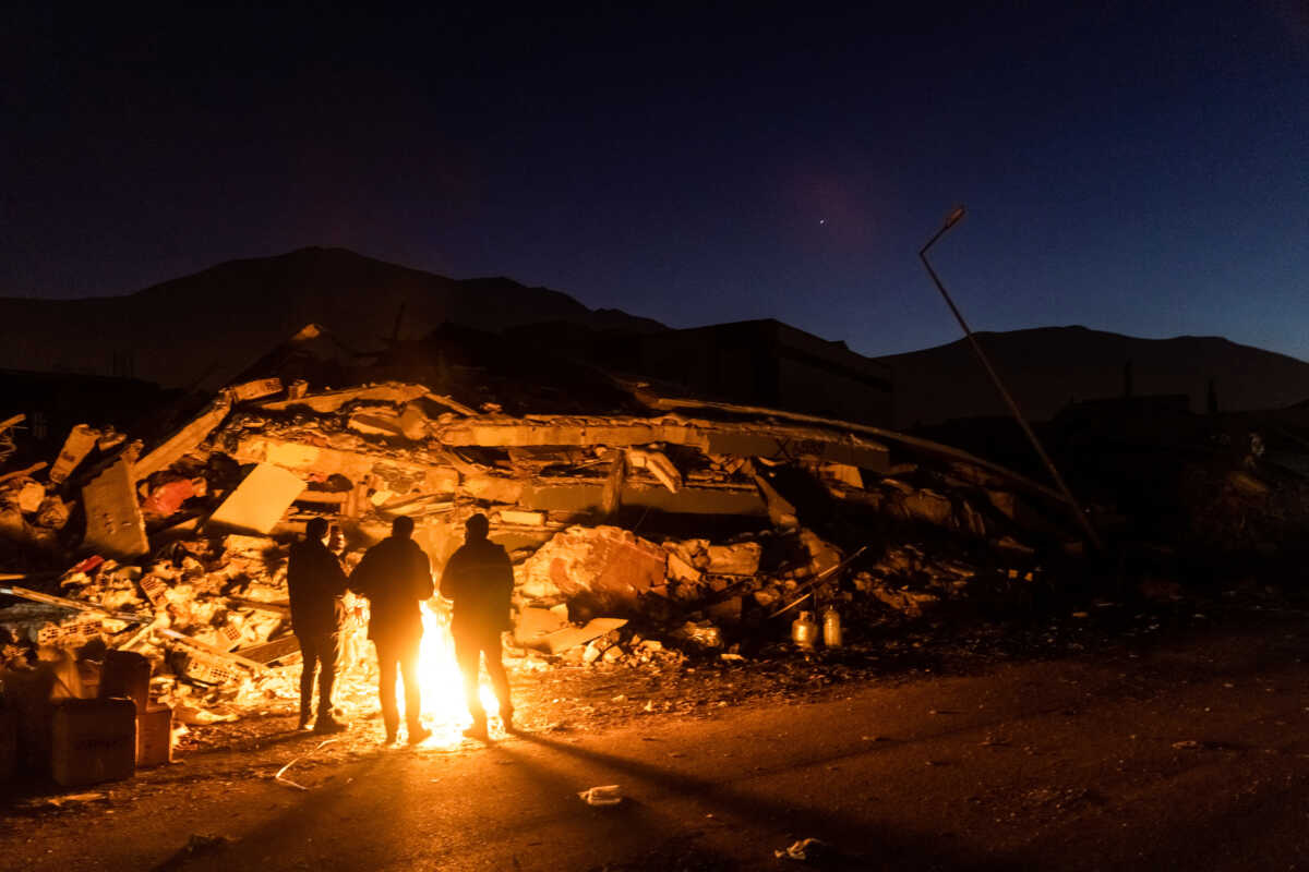 People stand by the fire next to remains of a destroyed building in the aftermath of a deadly earthquake in Elbistan, Turkey February 14, 2023. REUTERS