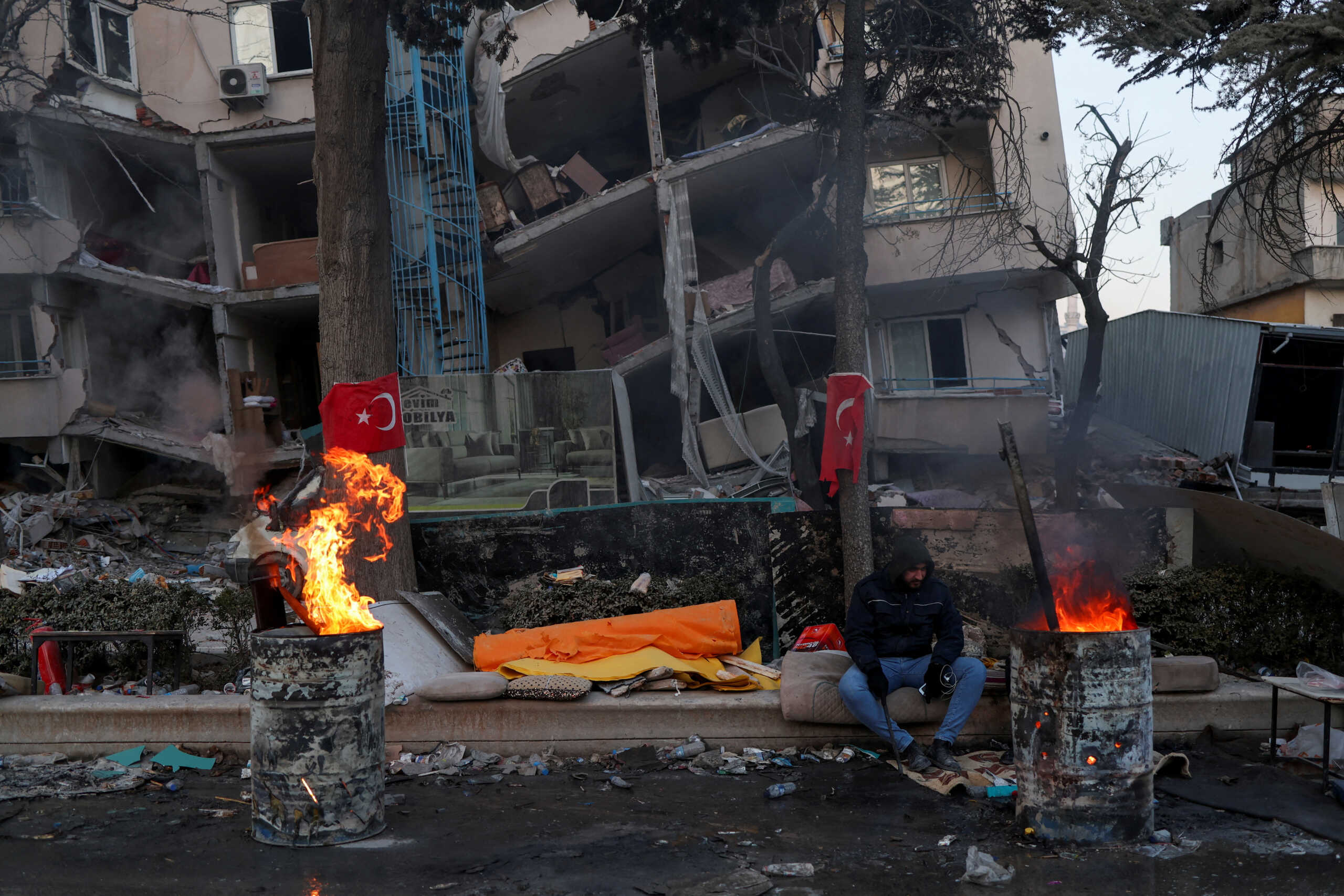 A man keeps warm by a fire in front of a damaged building in the aftermath of a deadly earthquake in Kahramanmaras, Turkey February 15, 2023. REUTERS