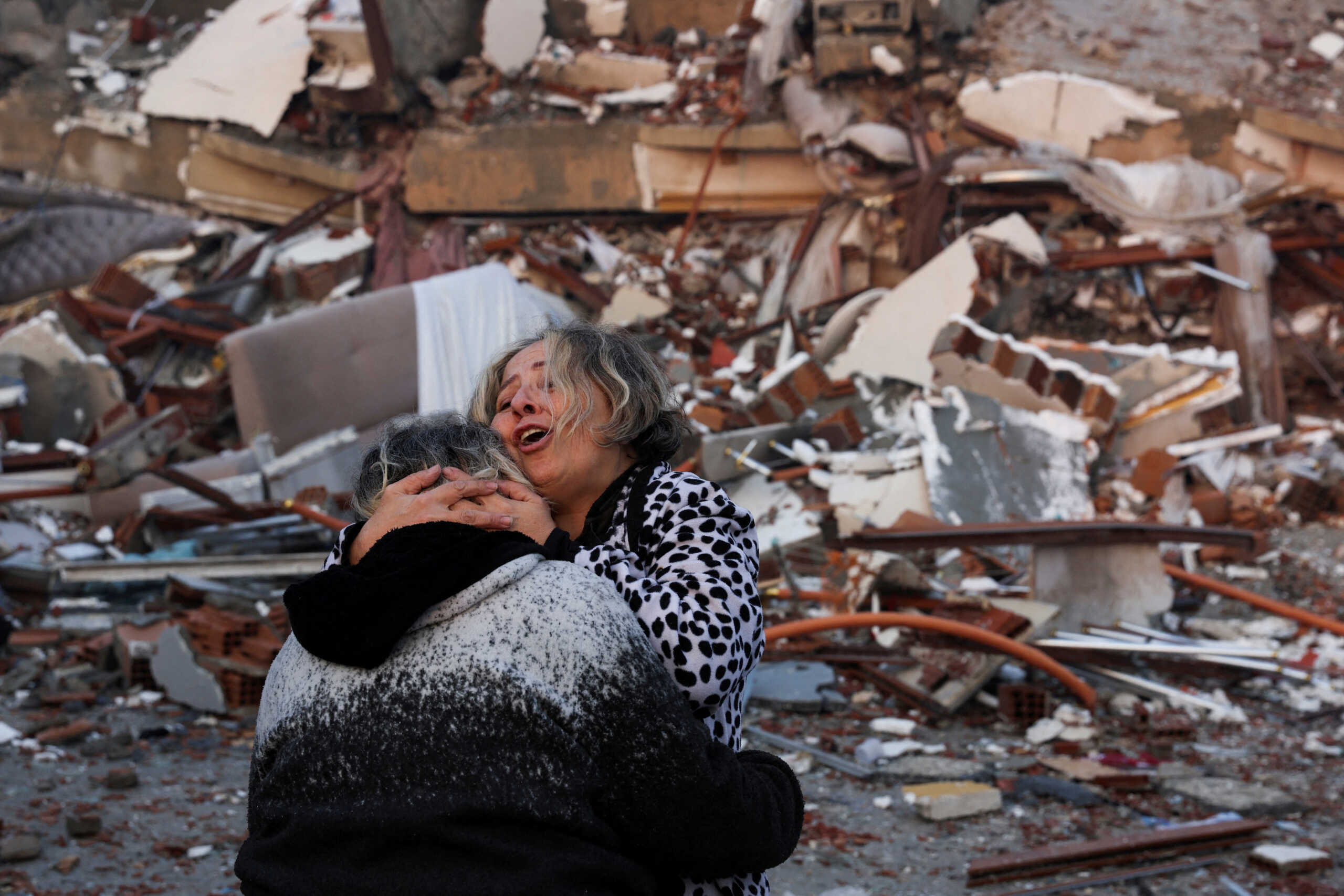 A woman reacts while embracing another person, near rubble following an earthquake in Hatay, Turkey, February 7, 2023. REUTERS
