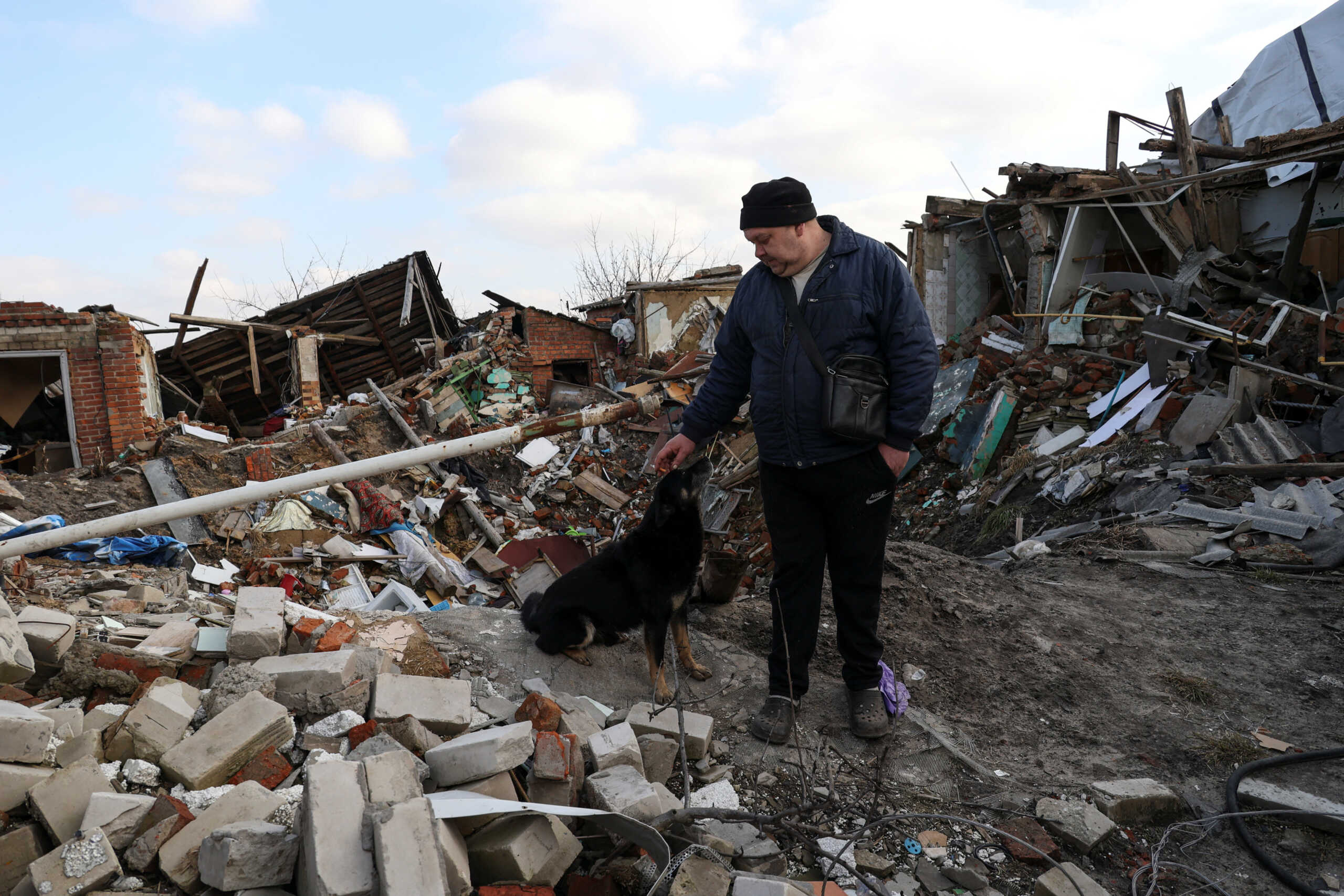 Local resident Volodymyr Alipov, 58, pets a dog among remains of his house destroyed last year by an airstrike during Russia's attack in the village of Tsyrkuny, Kharkiv region, Ukraine March 20, 2023. REUTERS