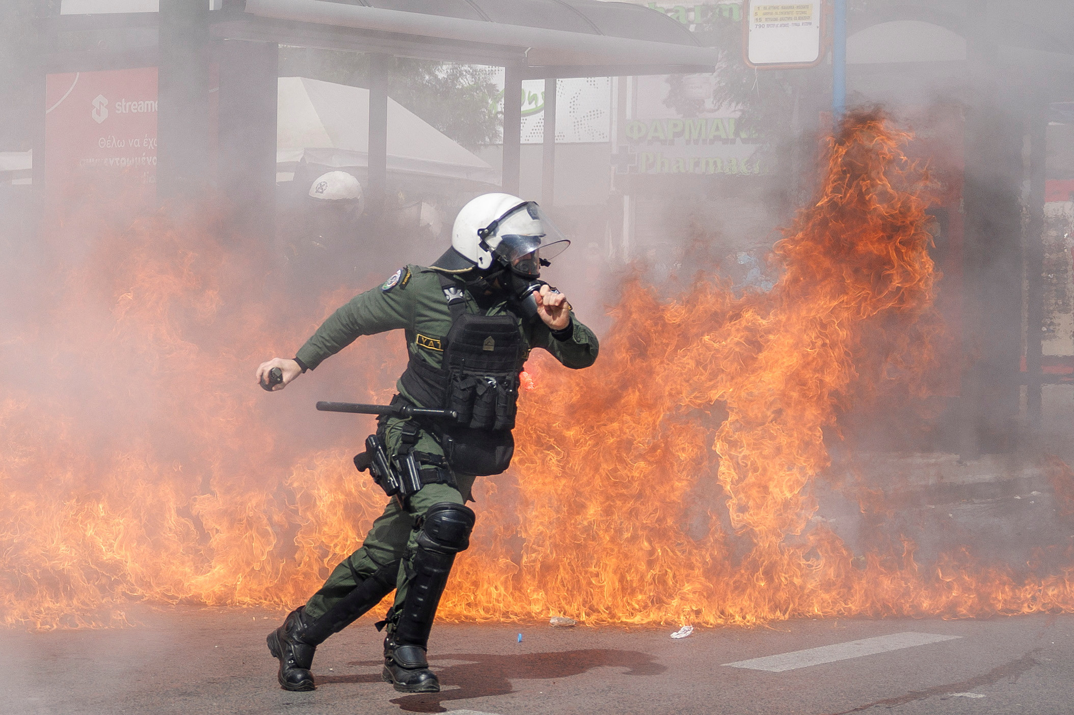 A riot police officer prepares to throw a stun grenade next to flames as clashes take place during a demonstration following the collision of two trains, near the city of Larissa, in Athens, Greece, March 5, 2023. REUTERS