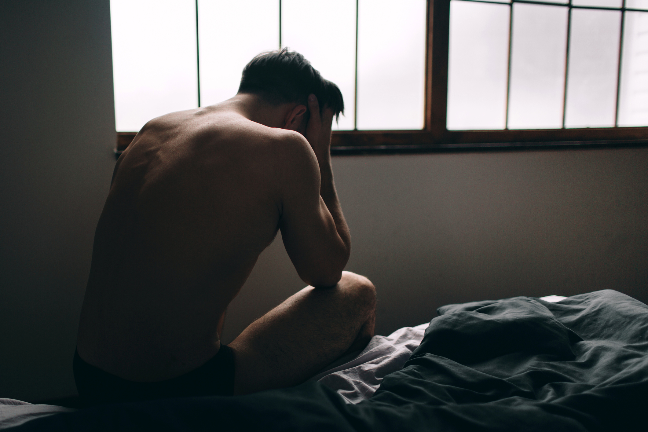 Depressed man sitting on bed in an empty room. This is major depressive disorder.