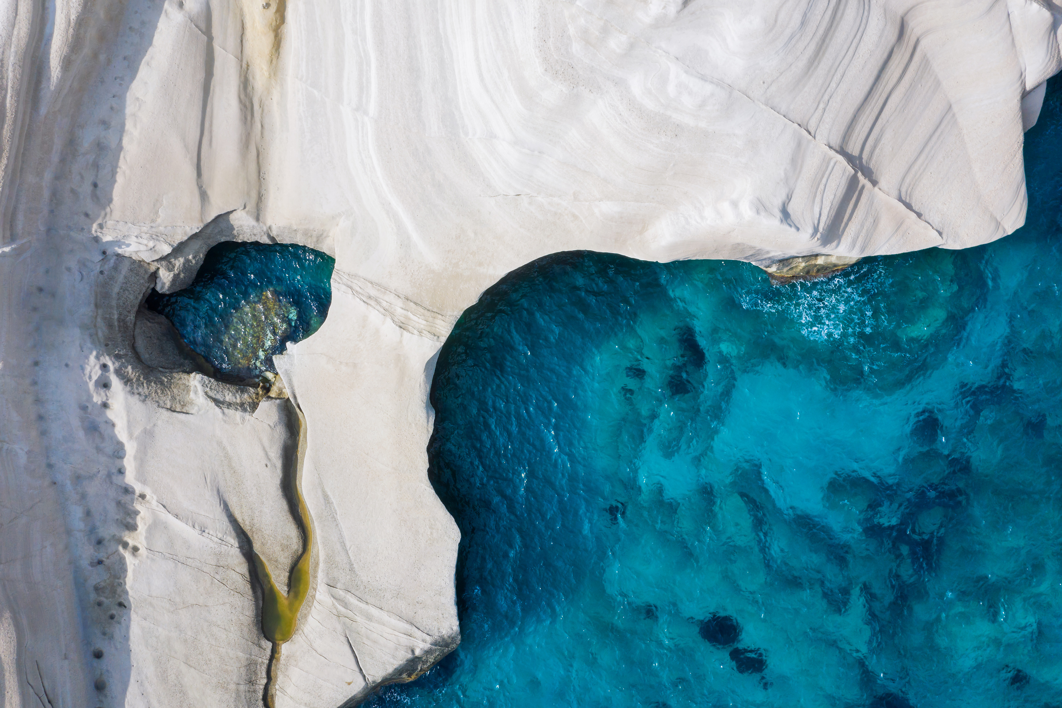 Aerial top down view to the chalk rock formations of Sarakiniko with sparkling blue sea, Milos island, Cyclades, Greece
