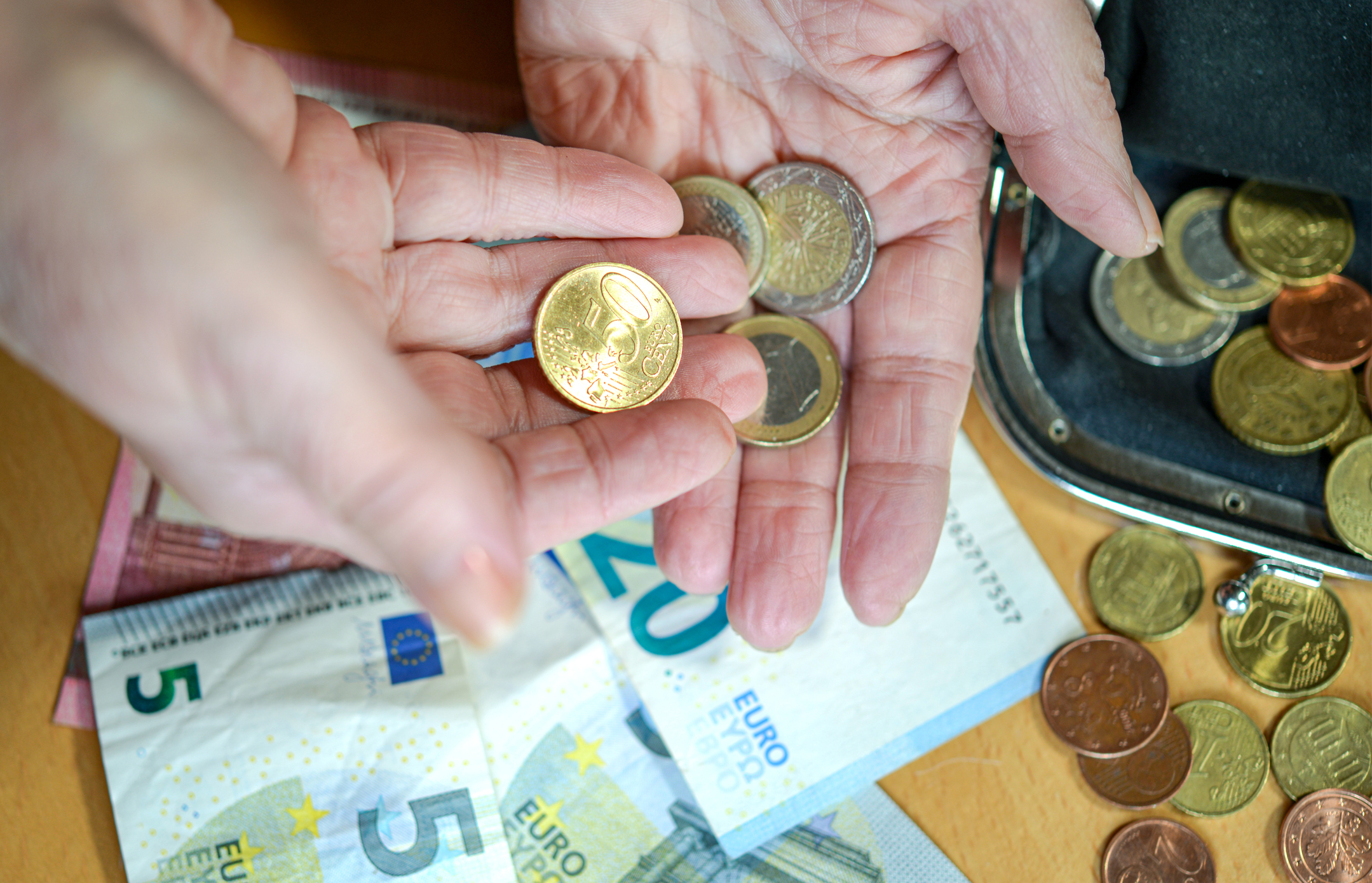 Elderly woman counts small change in her hand, bills are on the table - selective focus, high angle view