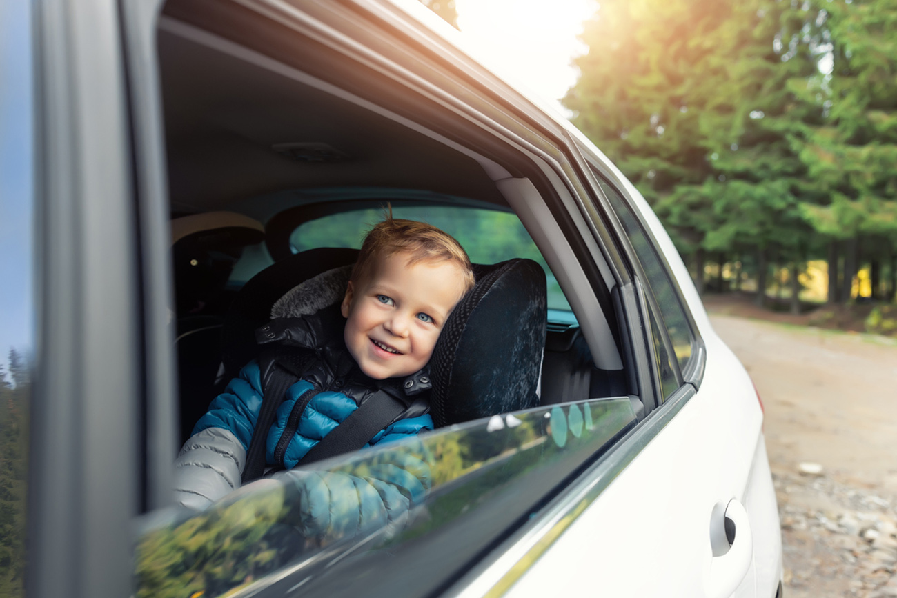 Little cute adorable happy caucasian toddler boy sitting in child safety seat car open window enjoy having fun making road trip nature countryside forest landscape. Family car travel by car concept.