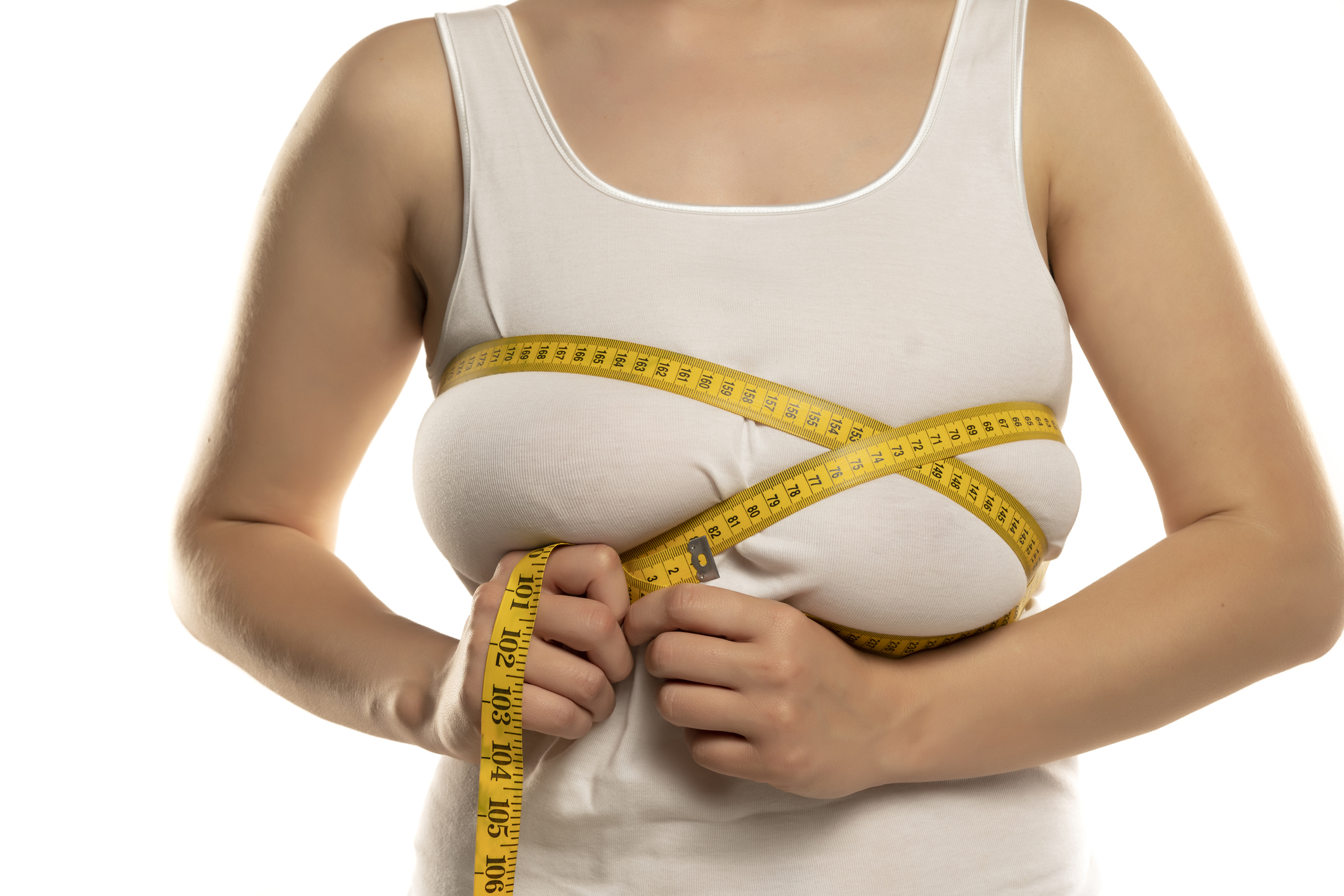 a woman measures with a measuring tape her large breasts on a white background