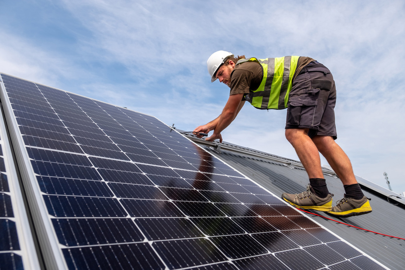 A young male carefully connects and installs solar panels on a residential rooftop. Houses in South Africa installing solar energy solutions