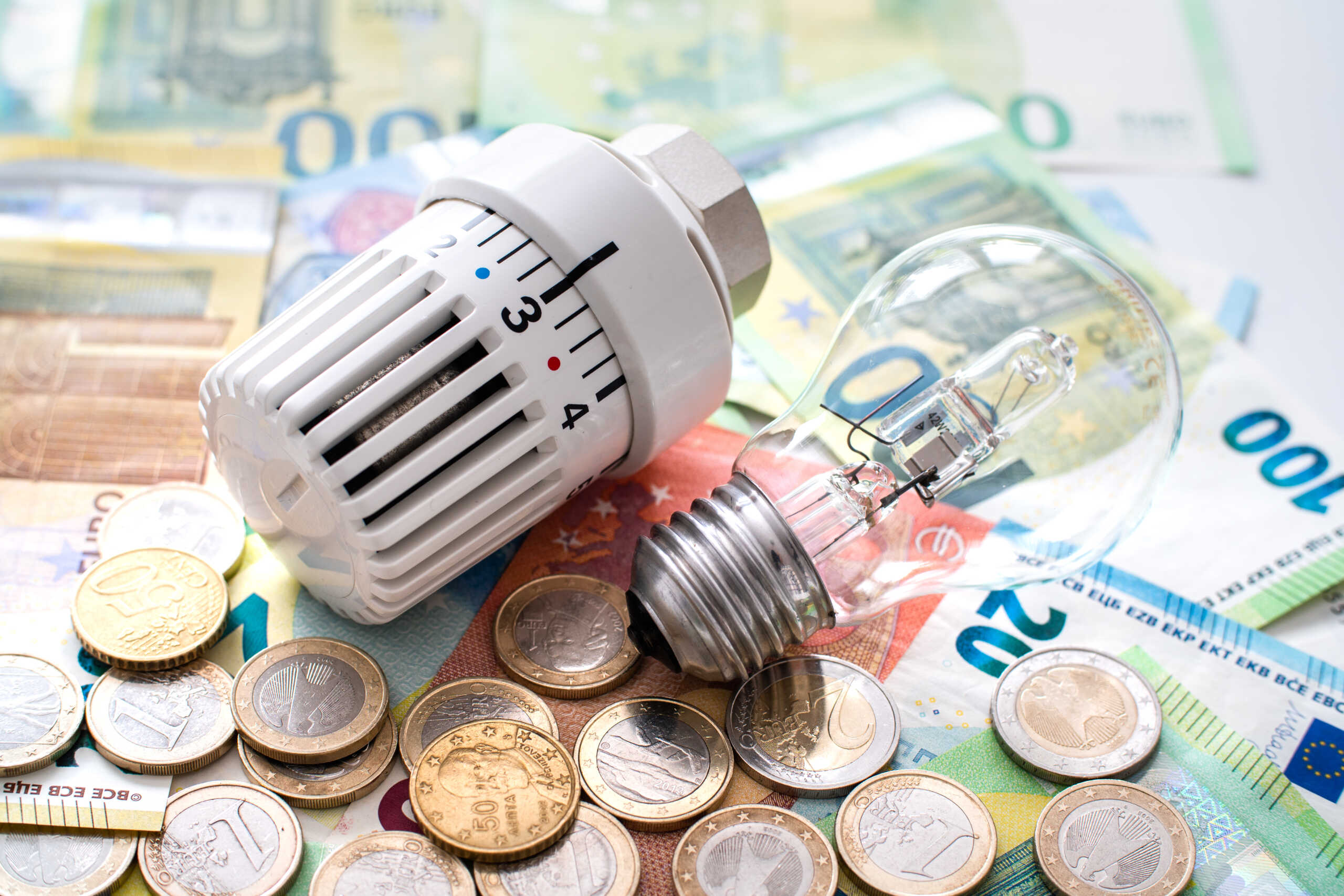 a heating valve and an old-fashioned lightbulb lie on top of euro bills and coins topic cost of energy supply
