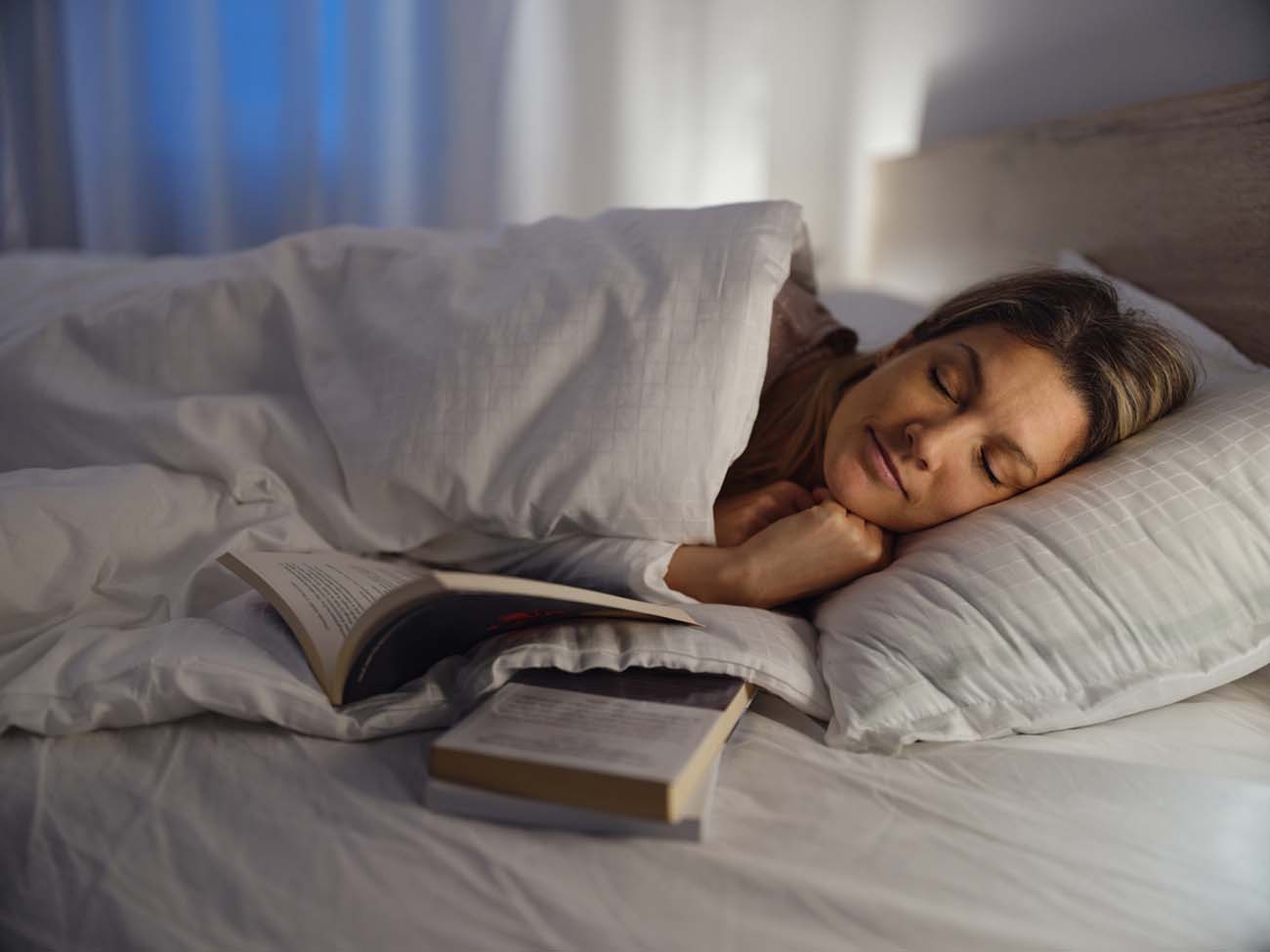 Young woman feel asleep after reading a book in bed at night.