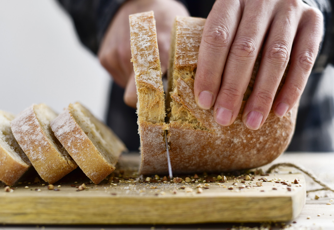 closeup of a young caucasian man cutting a loaf of bread in slices with a knife