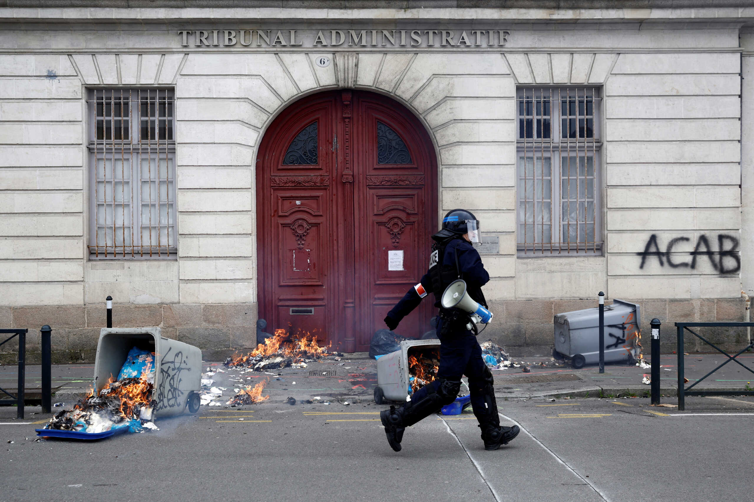 A French police officer runs past burning garbage bins in front of the entrance of the administrative court during clashes at a demonstration as part of the tenth day of nationwide strikes and protests against French government's pension reform in Nantes, France, March 28, 2023.   REUTERS