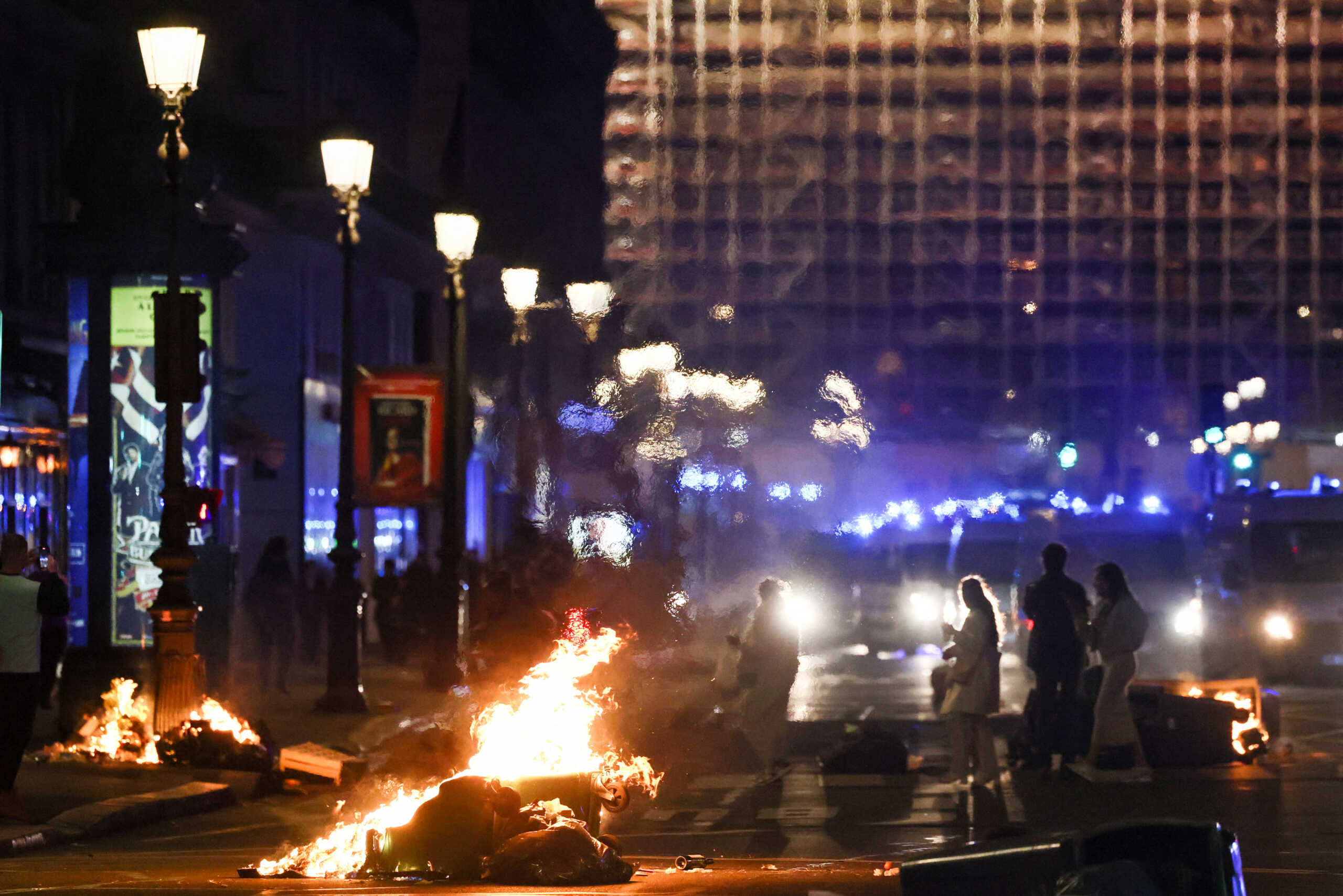 People walk past burning garbage bins near the Opera Garnier on the day the National Assembly debates and votes on two motions of no-confidence against the French government, tabled by centrist group Liot and far-right Rassemblement National party, for its use of article 49.3, a special clause in the French Constitution, to push the pensions reform bill through the National Assembly without a vote by lawmakers, in Paris, France, March 20, 2023. REUTERS