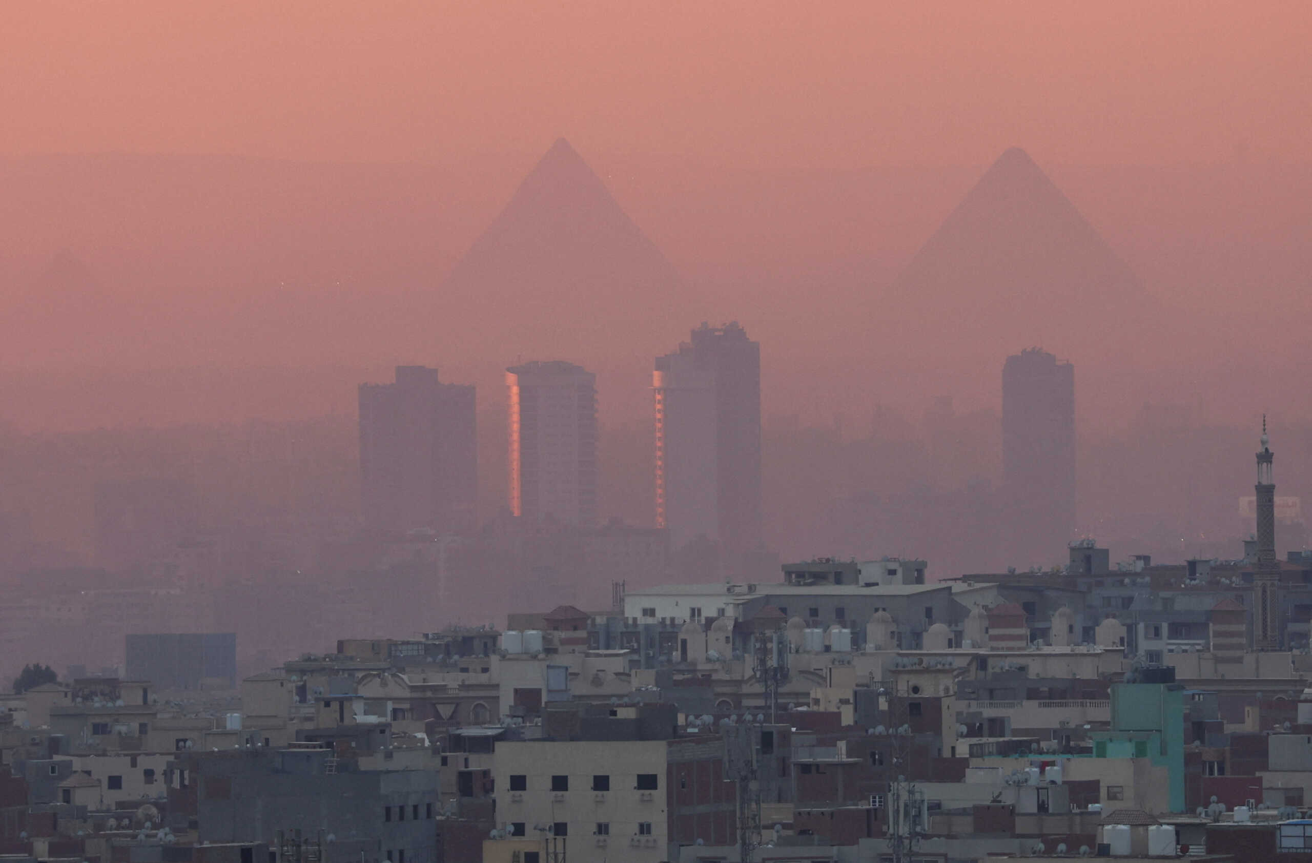 A view of old houses with hotels and the Great Pyramids during sunset with fog from air pollution over the Egypt's capital of Cairo, Egypt February 5, 2023. REUTERS