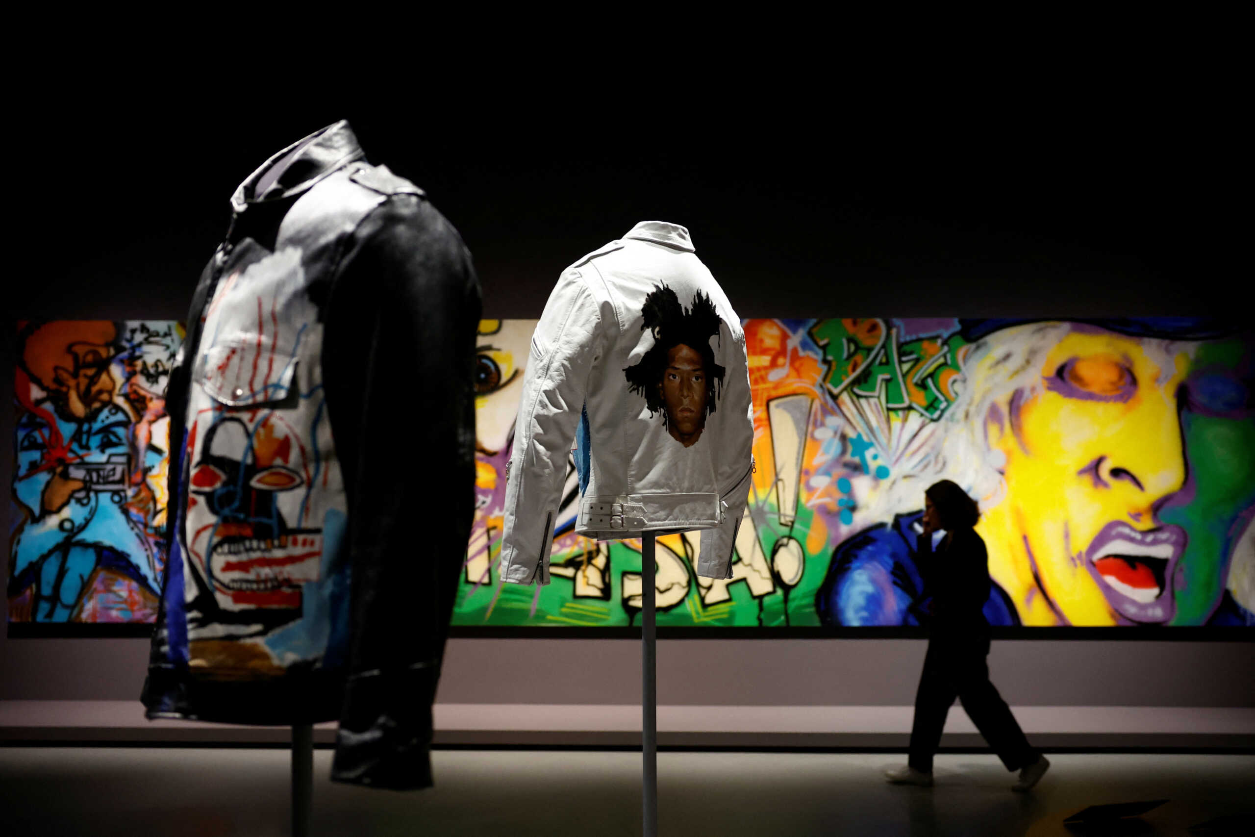 A woman walks behind the artworks "Leather Jacket" (1985) by artists Jean-Michel Basquiat (1960-1988) and Stefano Castronovo during a press visit of the exhibition "Basquiat x Warhol, Painting Four Hands" at the Fondation Louis Vuitton in Paris, France, April 4, 2023. REUTERS