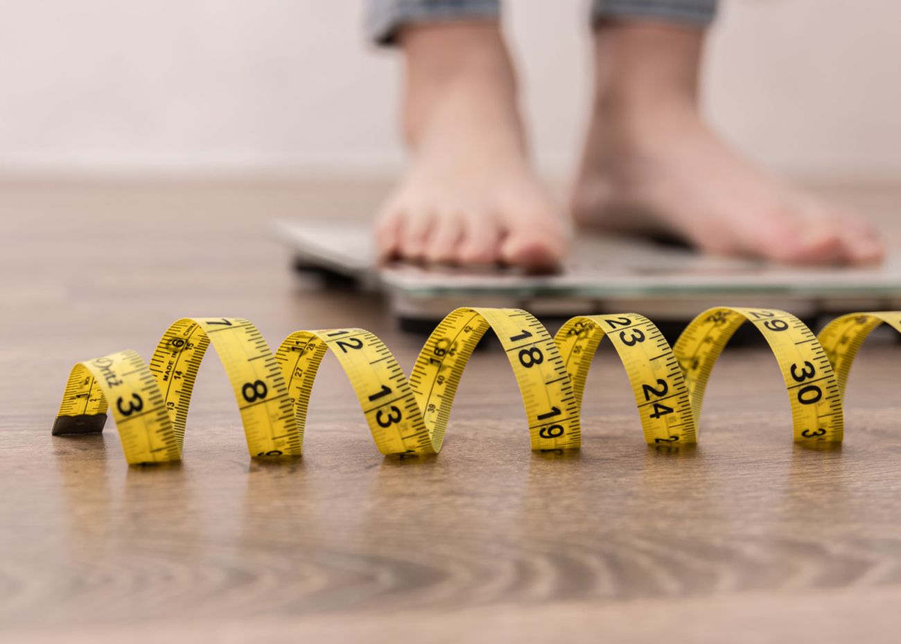 Women's legs on the scales, close-up of a measuring tape, the concept of losing weight, healthy lifestyle.