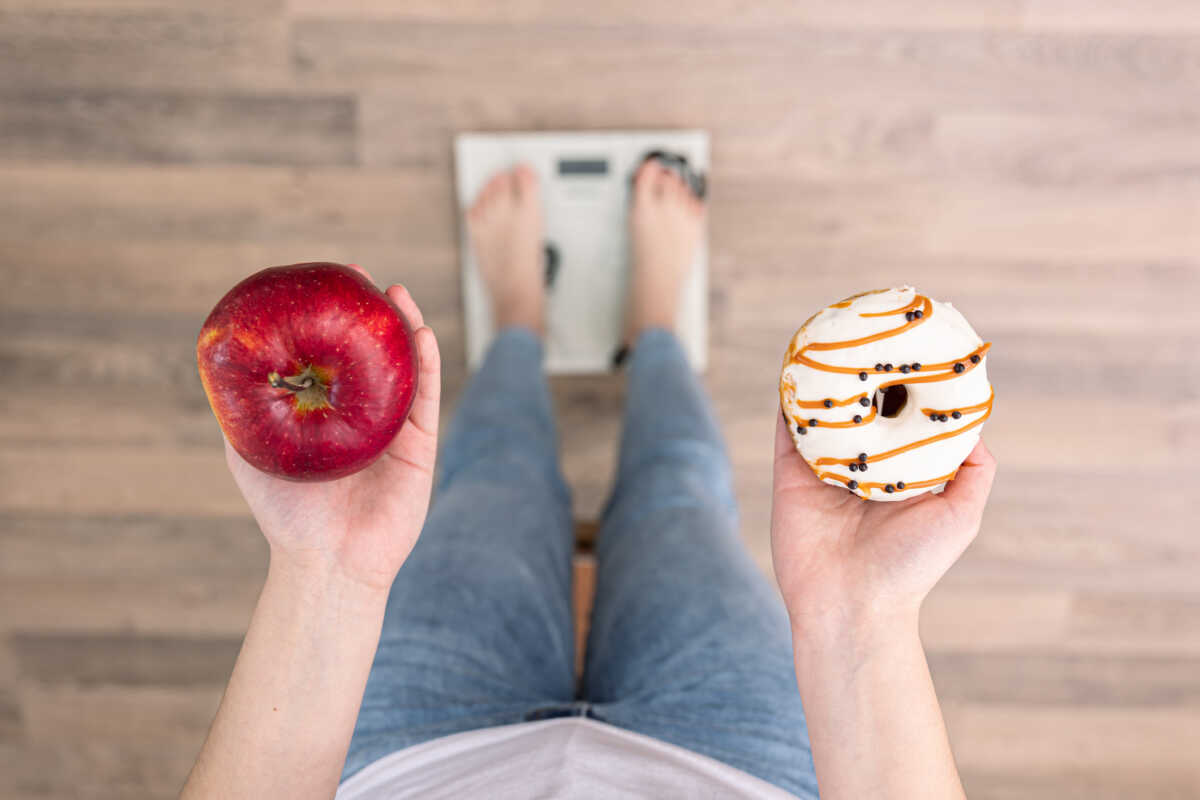 A woman stands on the scales, holds a donut and an apple in her hands, the concept of diet, weight gain, weight loss, proper nutrition, obesity.