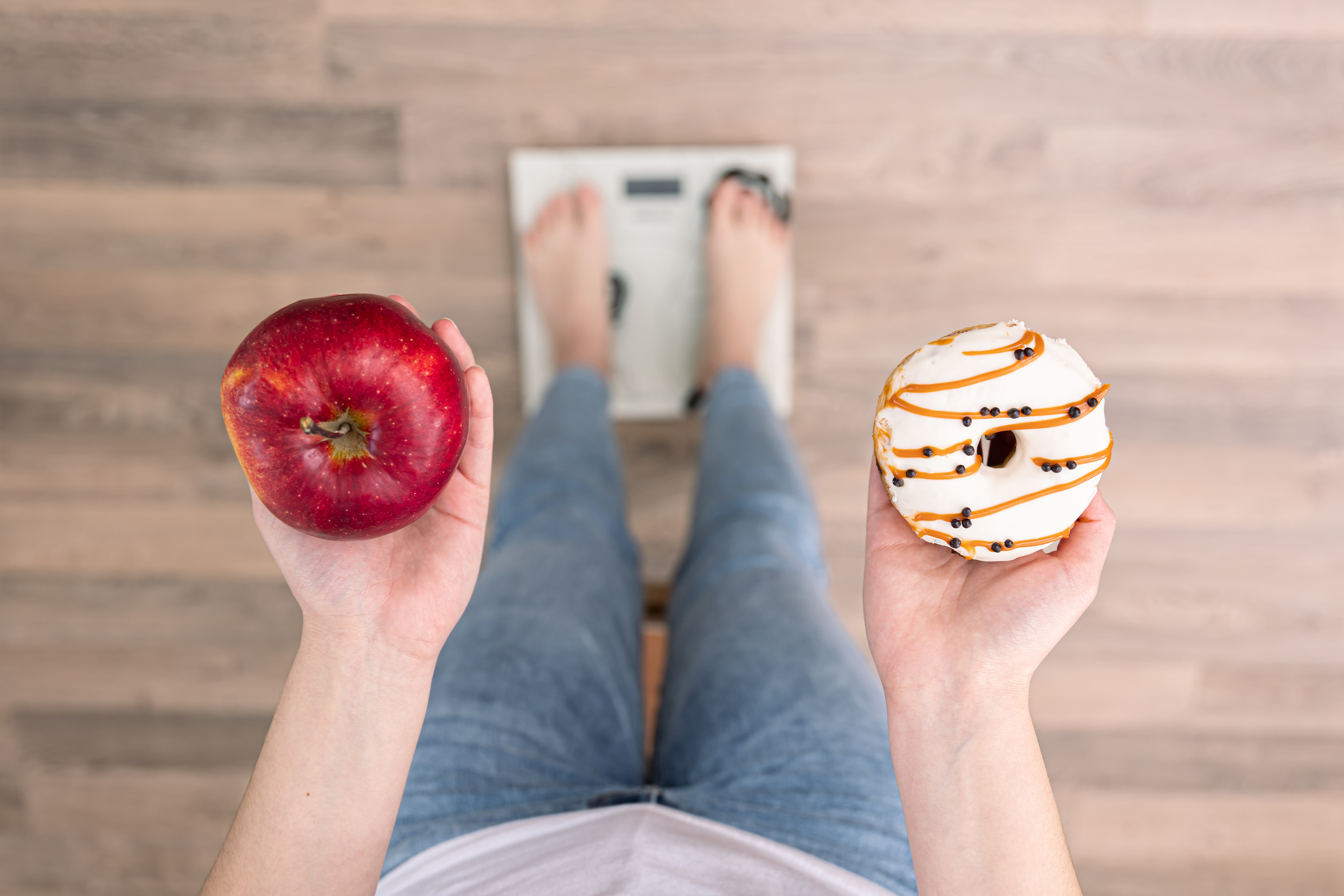 A woman stands on the scales, holds a donut and an apple in her hands, the concept of diet, weight gain, weight loss, proper nutrition, obesity.