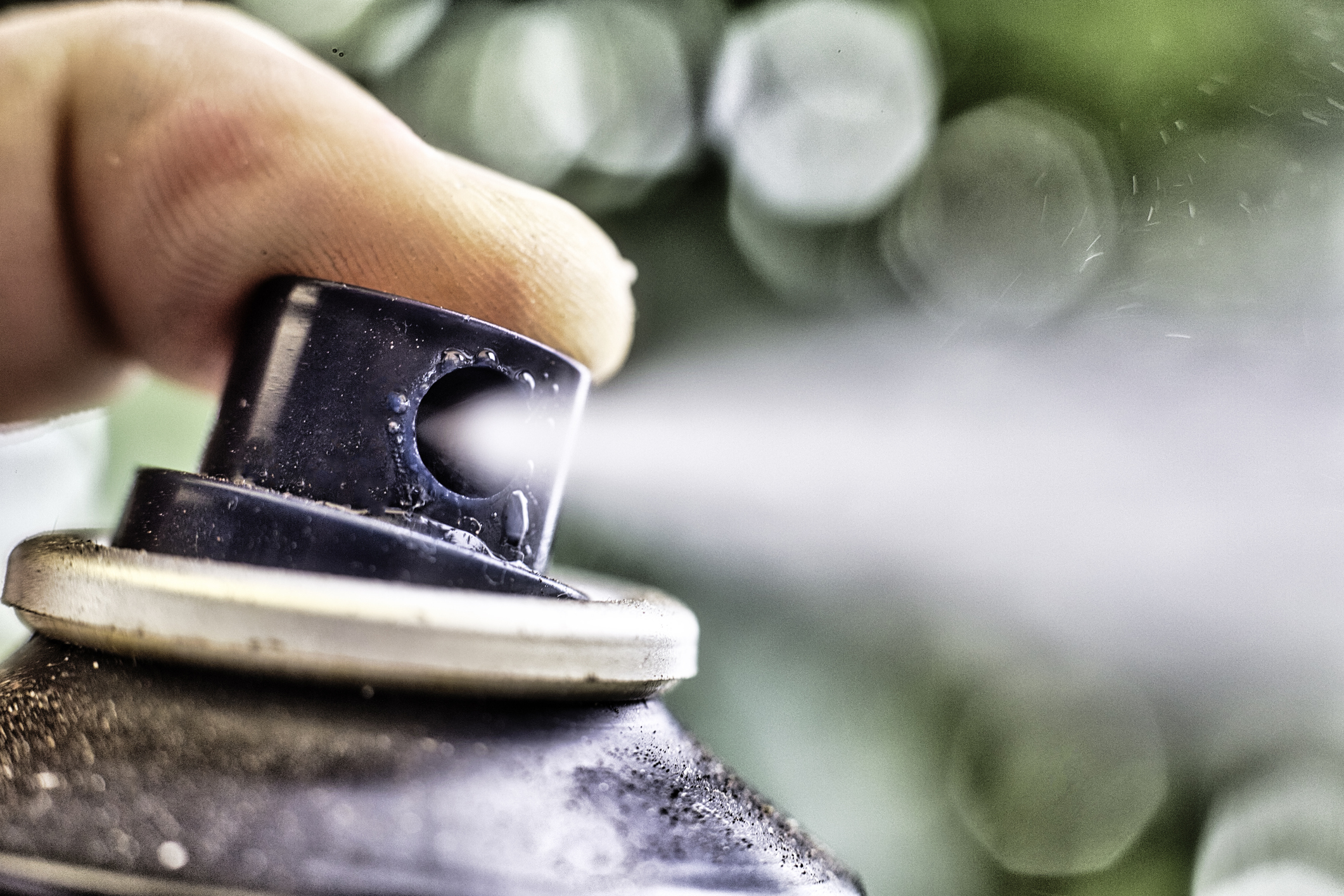 A finger presses the nozzle on an aerosol can causing a spray