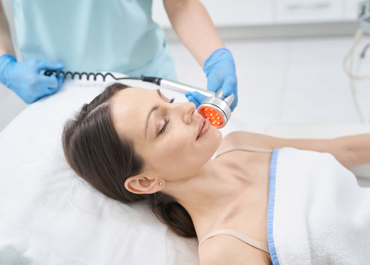 Doctor beautician using radiofrequency device while performing skincare procedure for client in beauty salon