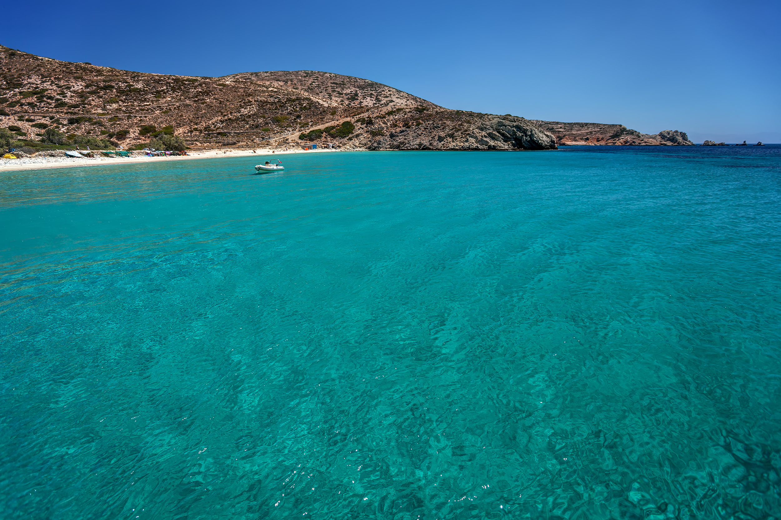 Sandy beach with transparent waters with a small anchored boat, in Donousa island, Cyclades, Greece.