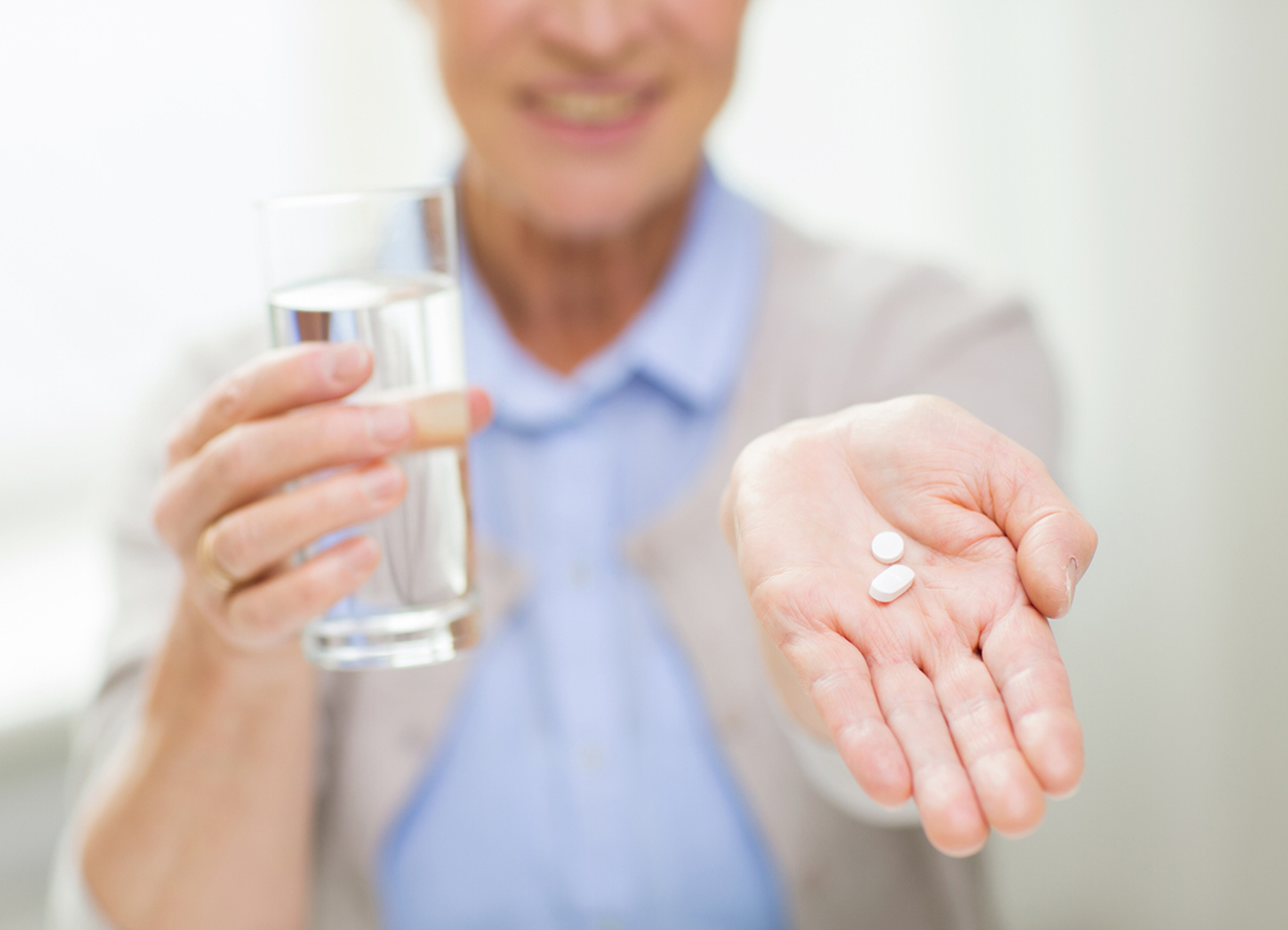age, medicine, health care and people concept - close up of happy senior woman with pills and glass of water at home