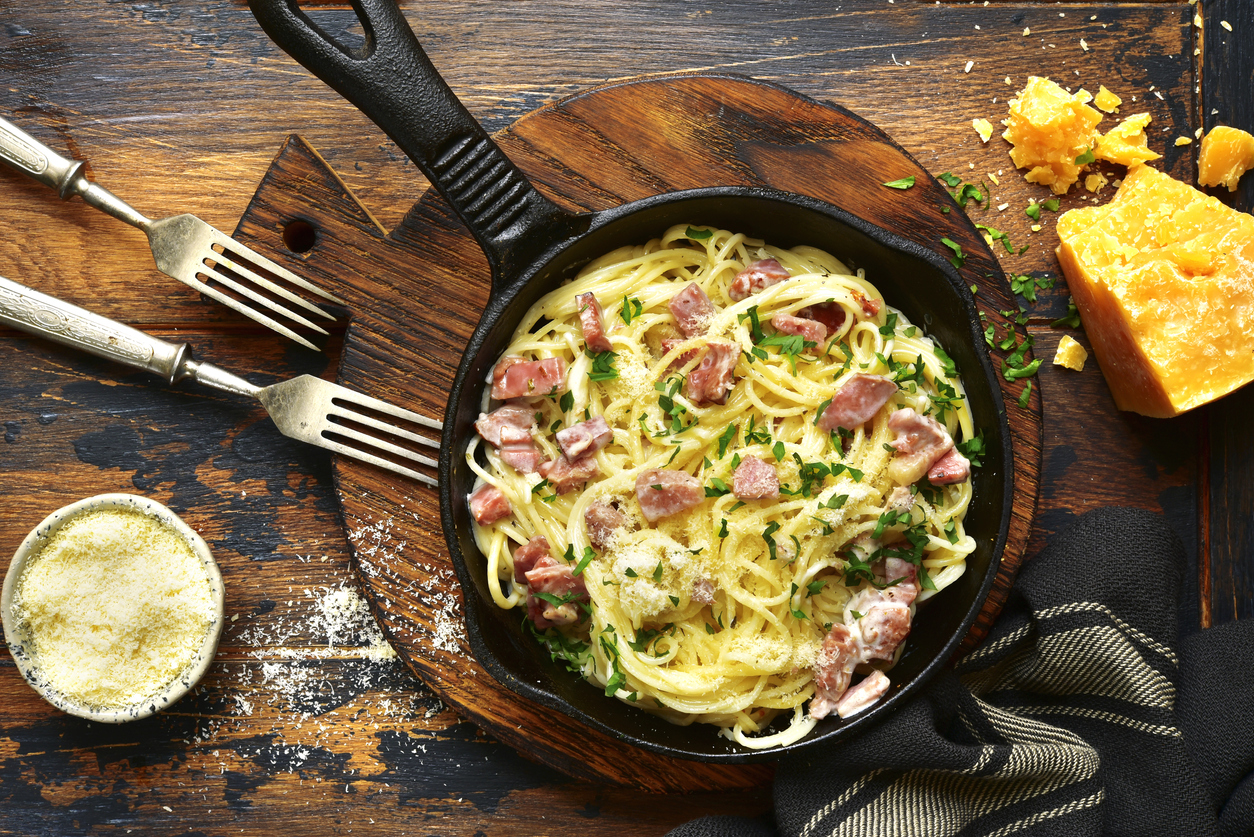 Traditional italian dish spaghetti carbonara with bacon in a cream sauce in a skillet over dark wooden background.Top view with copy space.