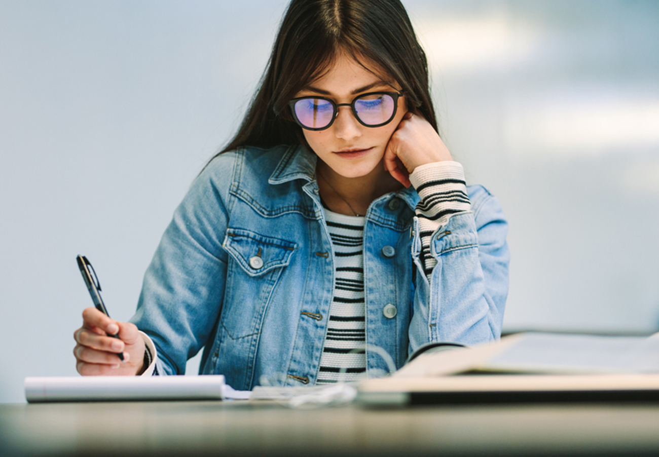 Woman student sitting at college library and studying. Girl reading notes at college campus.