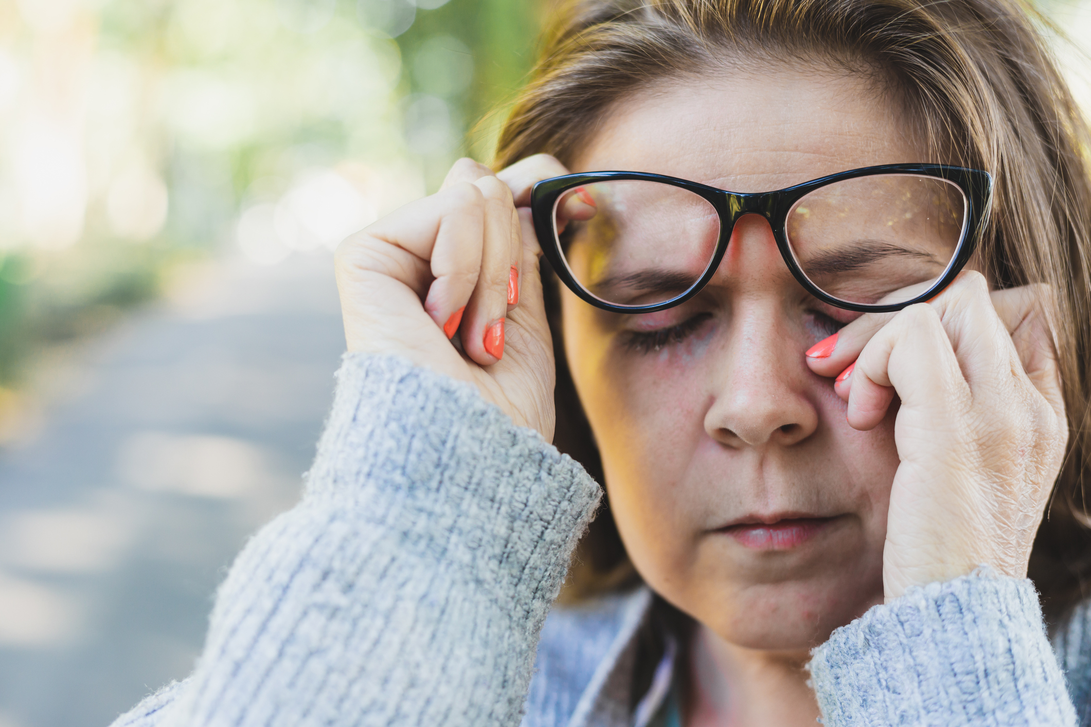 Close up shot of young woman rubbing her eye with one hand outdoors - Portrait of cute and sleepy girl with brown hair wearing eyeglasses
