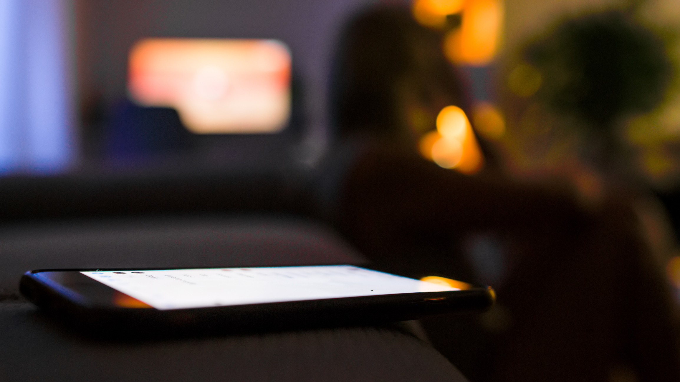 Depressed woman sitting on floor with mobile phone on sofa during night