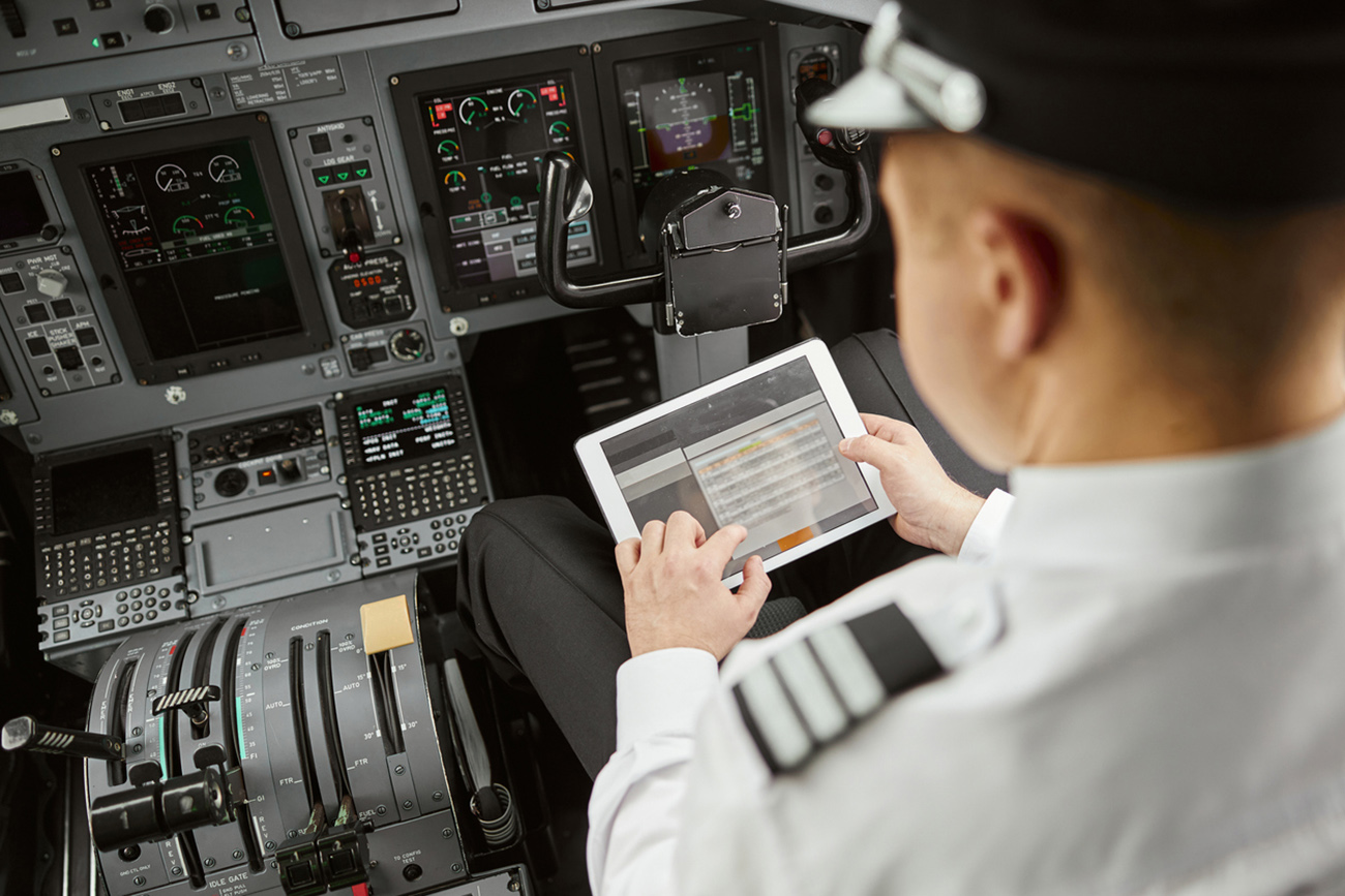 Male pilot use digital tablet in passenger airplane jet. Interior of cockpit in modern plane with dashboard and air navigation. Top view of man wear uniform. Civil aviation. Air travel concept