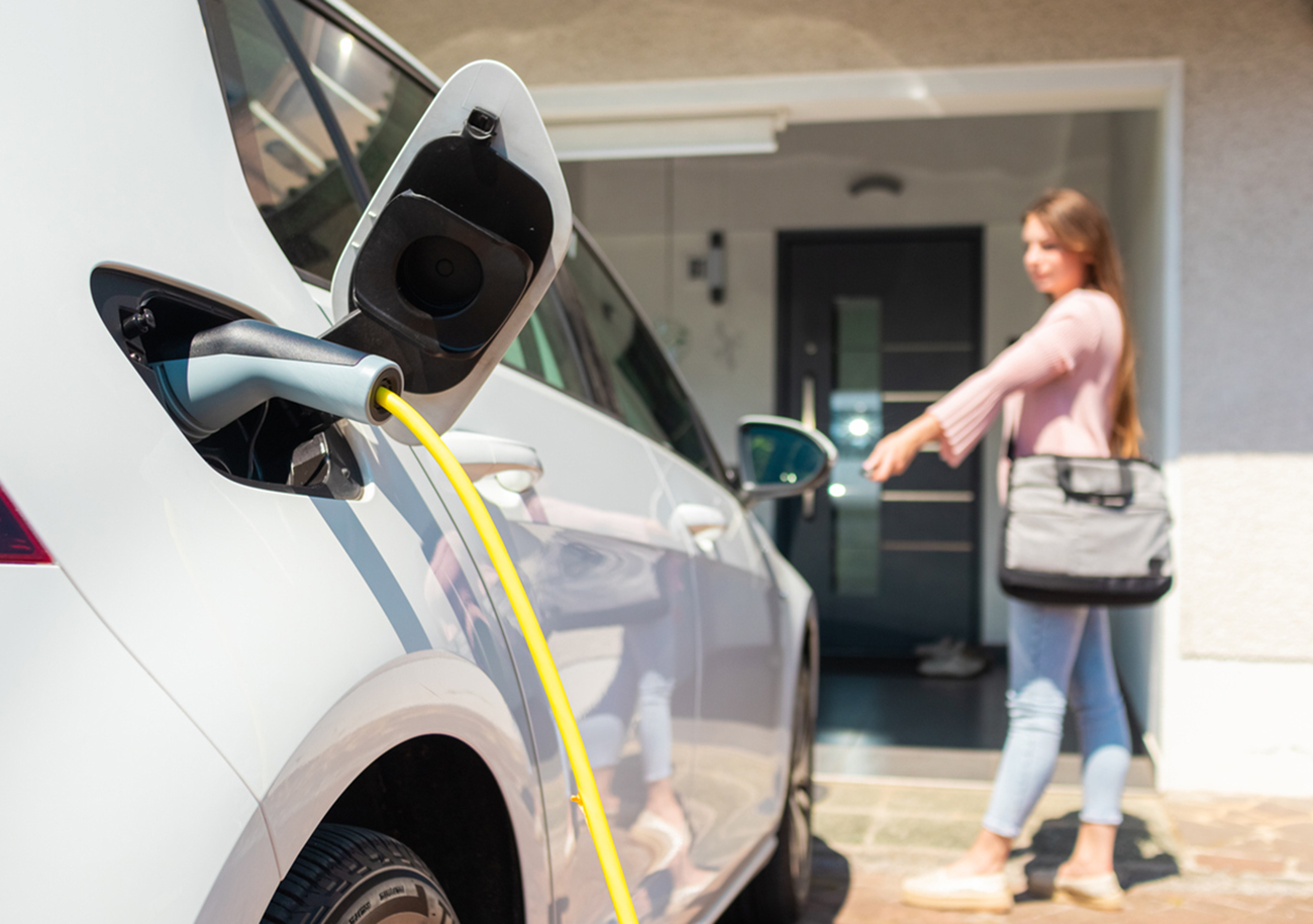 Woman charging electric car at home with cable.