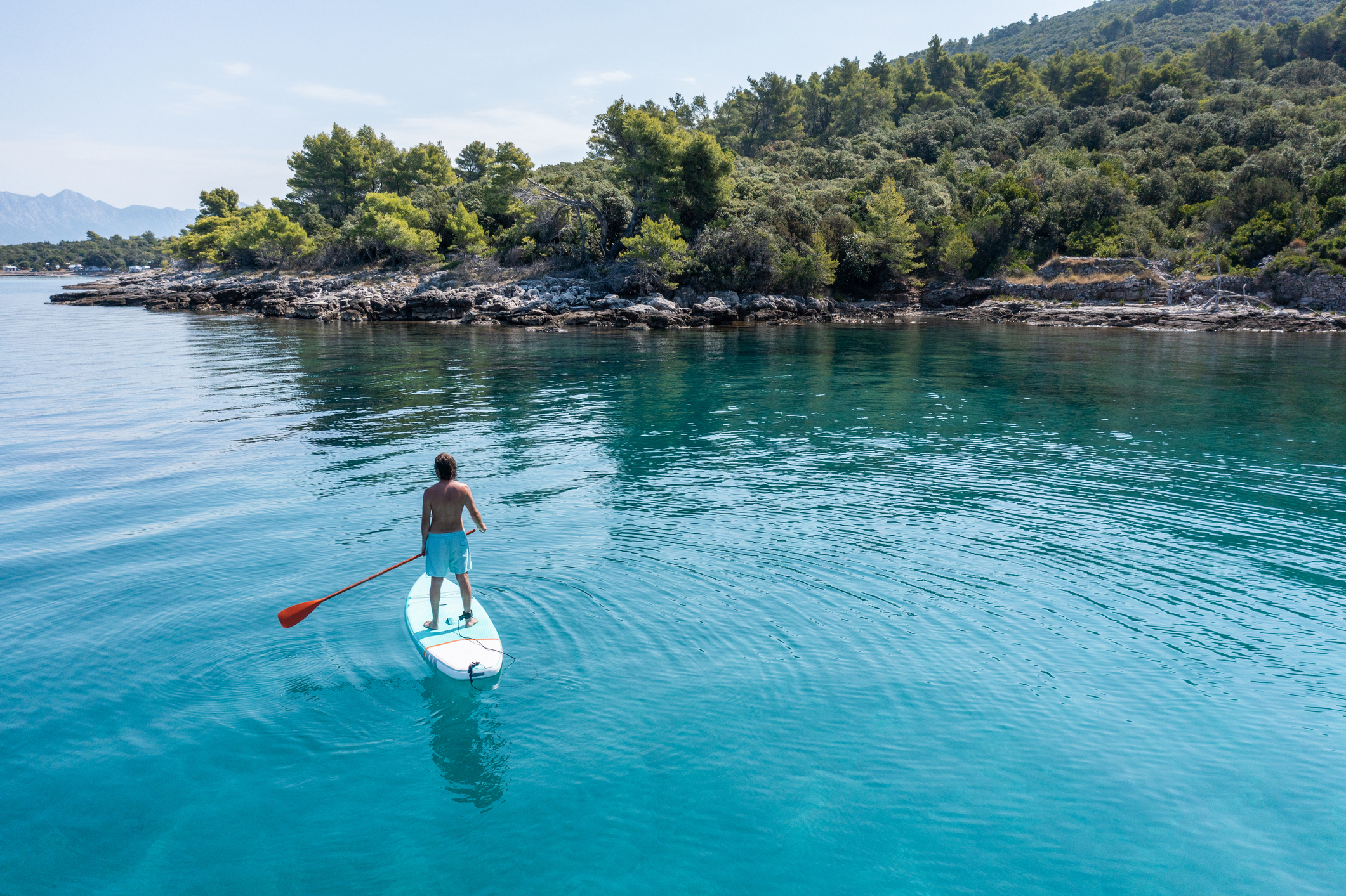 He stands on paddle board and enjoys relaxation on tropical turquoise lagoon