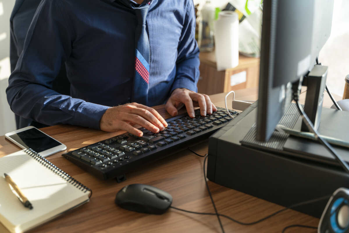 ofis masasında çalışan memur arka planı. masaüstü bilgisayar, klavye, not defteri, cep telefonu, bilgisayar faresi klavyede yazan insan eli görüntüsü full frame makine ile çekilmiştir