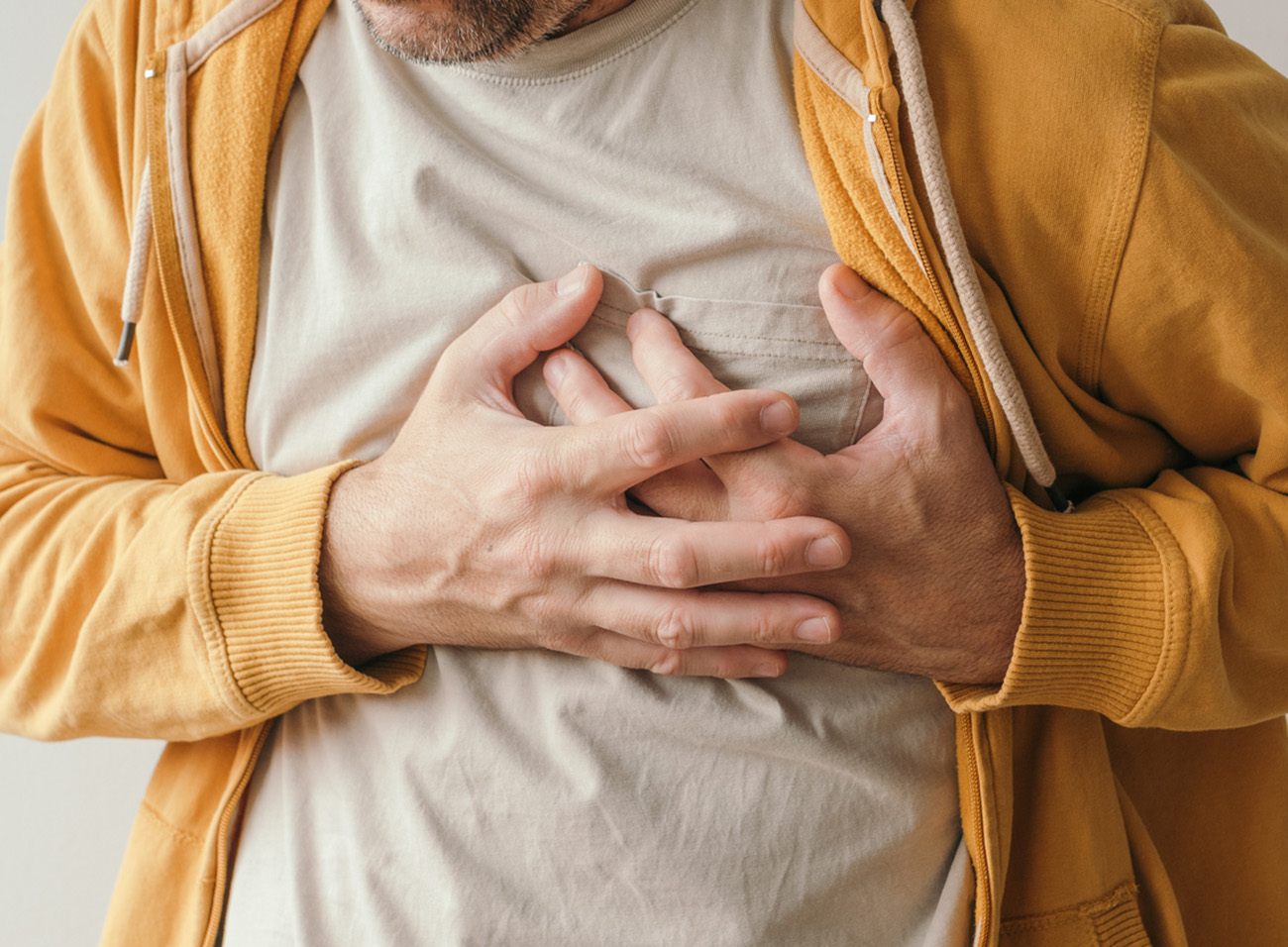 Aching heart and heart attack, adult male with painful grimace pressing the upper abdomen with his hands to ease pain