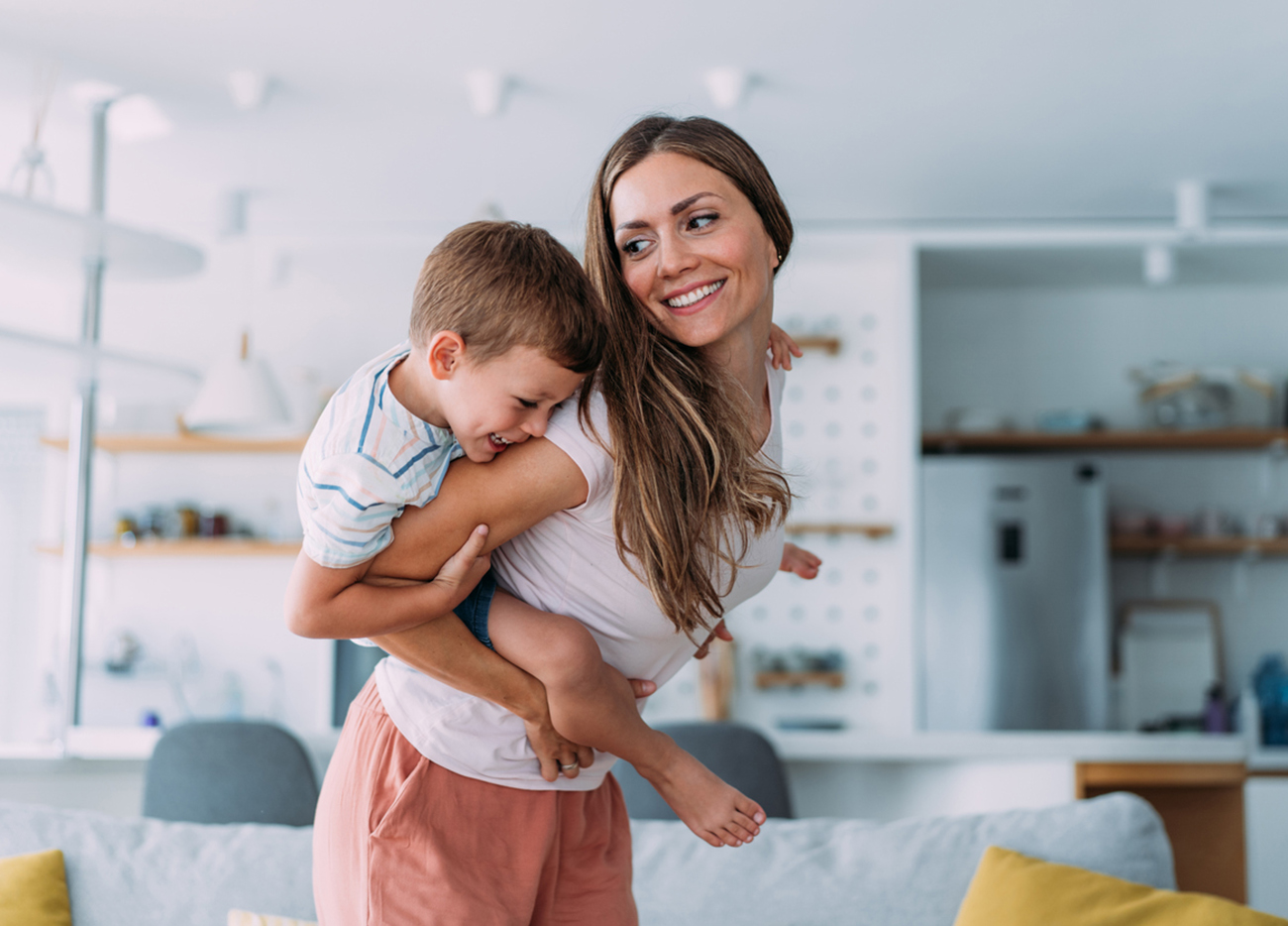 Shot of a mother and her cute little boy spending time together at home. Happy single mother and son having fun in the living room. Portrait of a mother giving her son a piggyback at home.
