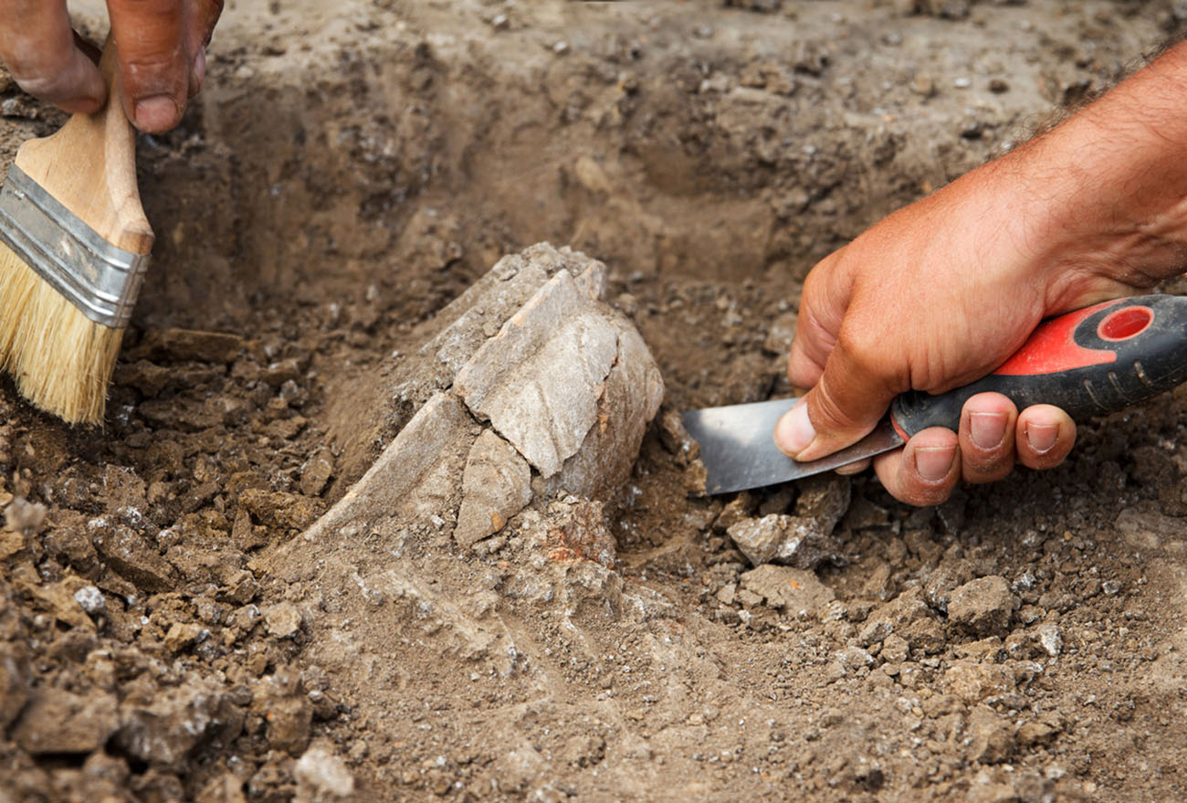 Archaeological excavations, archaeologists work, dig up an ancient clay artifact with special tools in soil