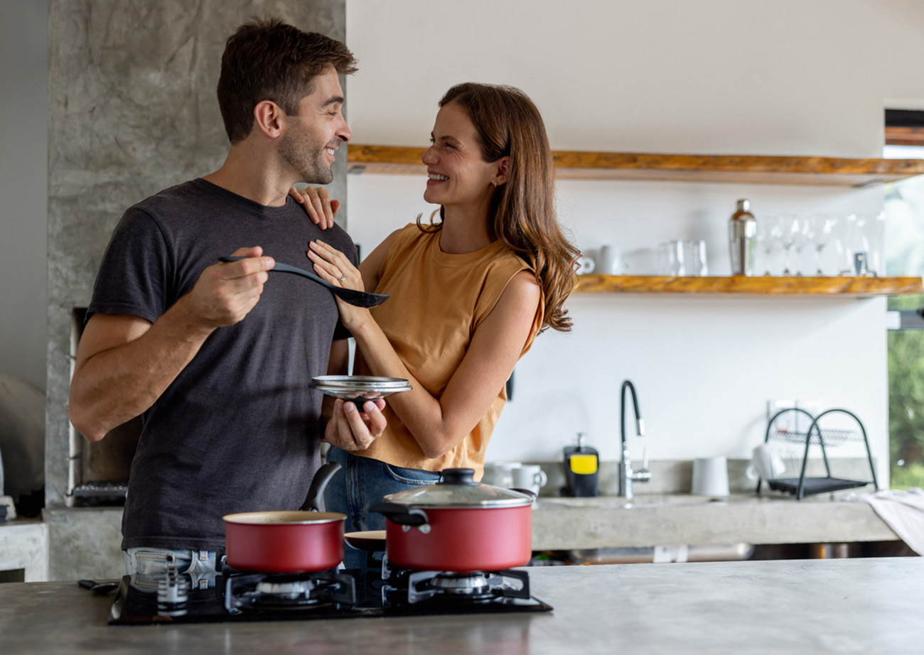 Loving Brazilian couple looking very happy cooking dinner together and smiling at each other