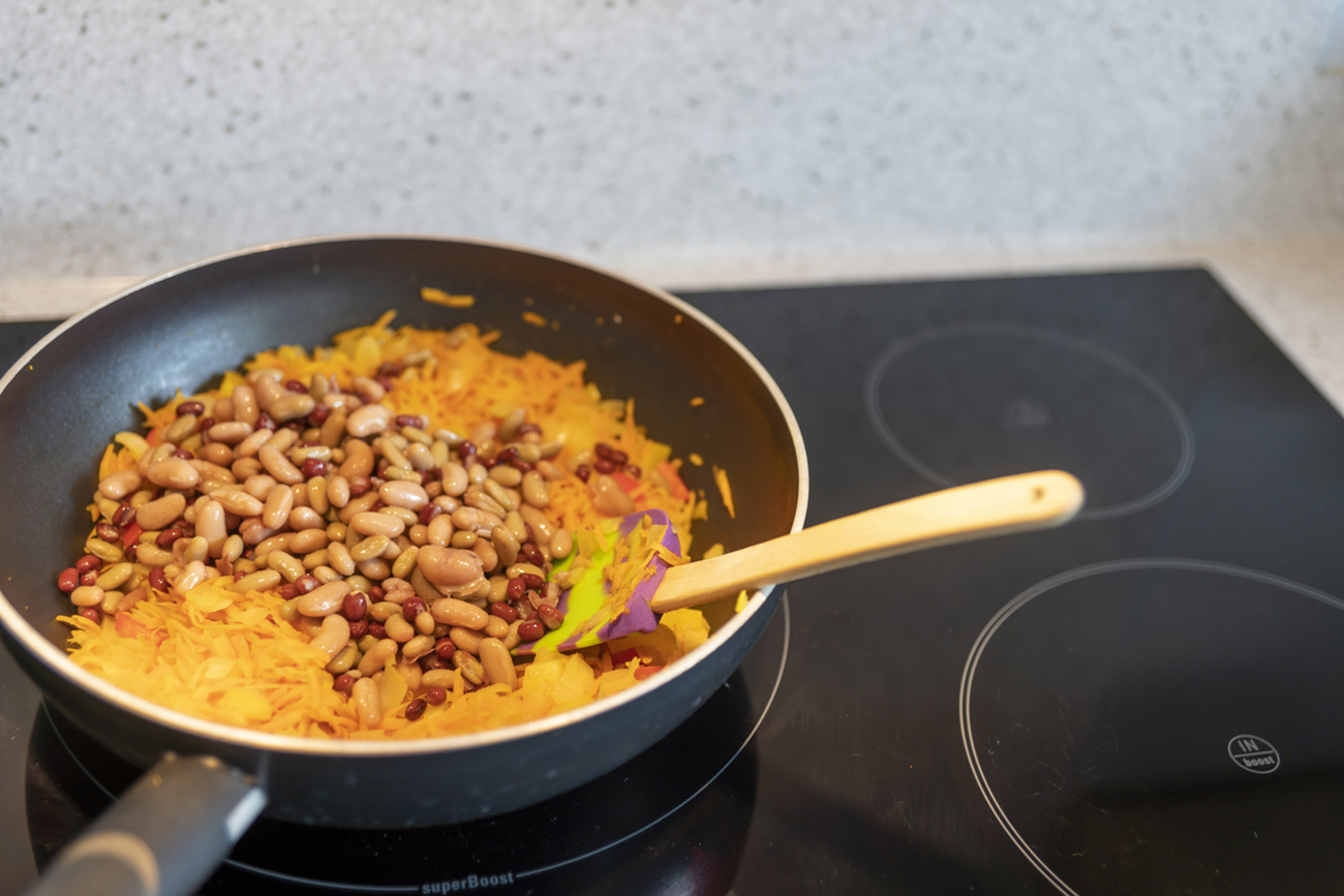 Cooking vegetarian enchilada filling on an induction hob in a modern kitchen.