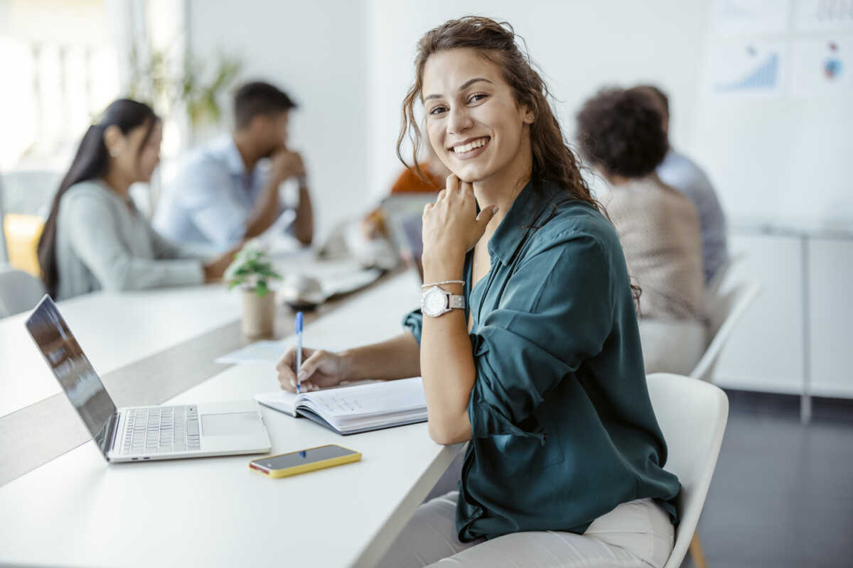 Female Employee Smiling in the Office, With Her Colleagues in Background. Shallow Focus