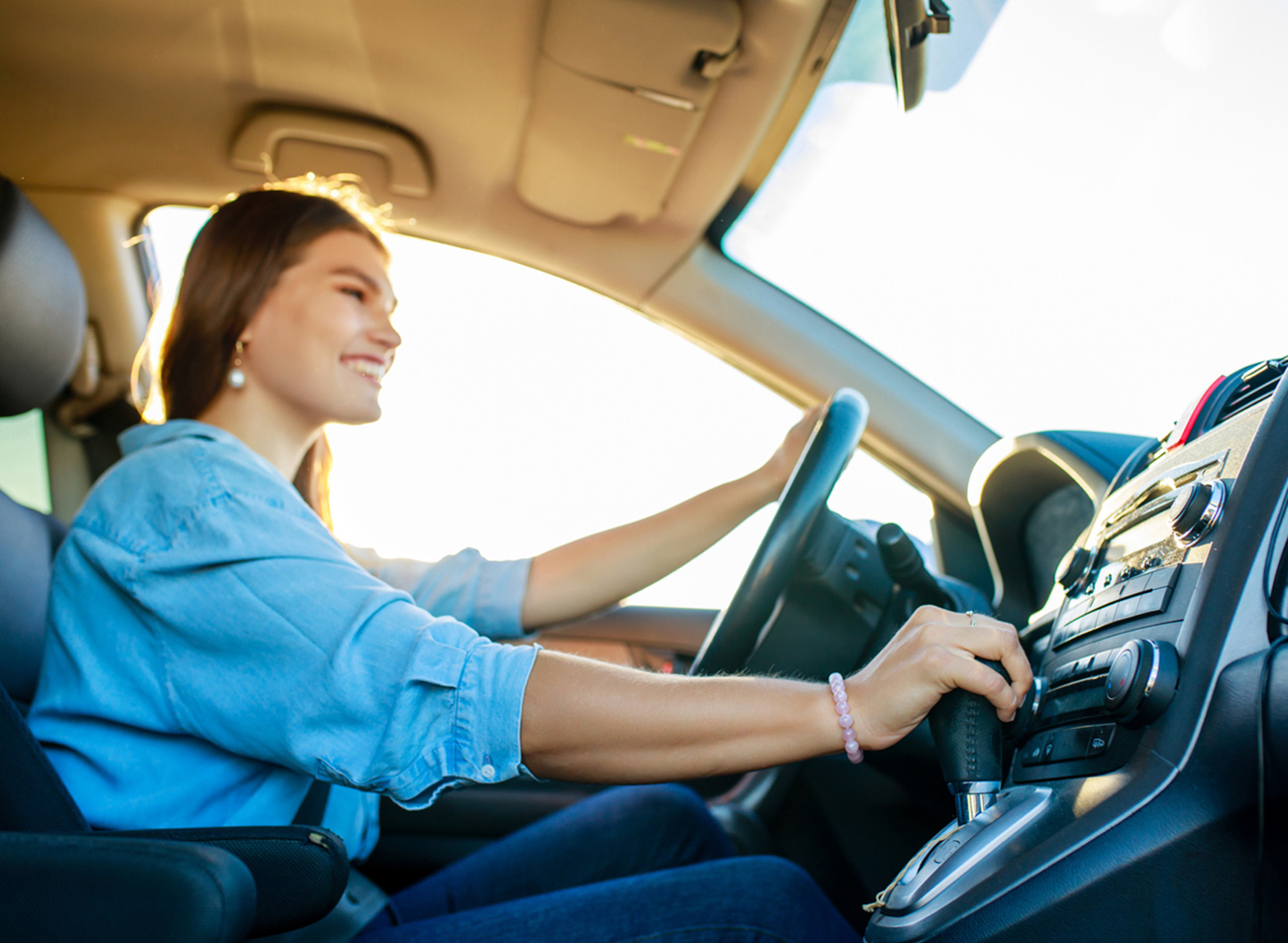 pretty woman singing while driving a car on road trip on summer day.