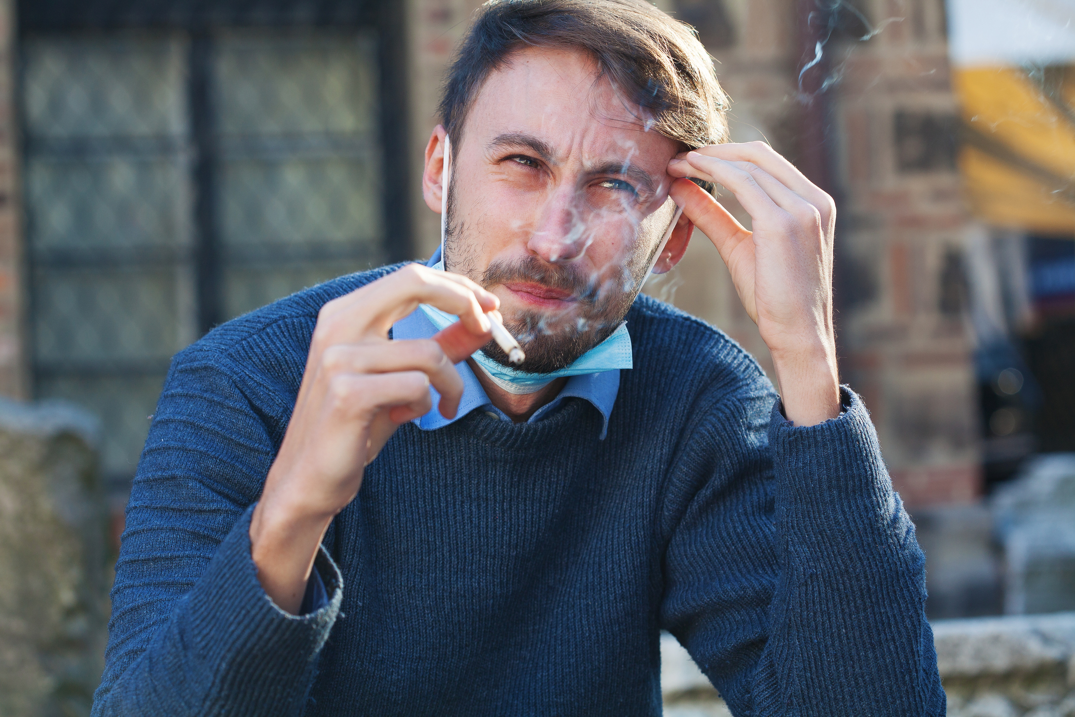 Young man with a protective face mask smoking a cigarette